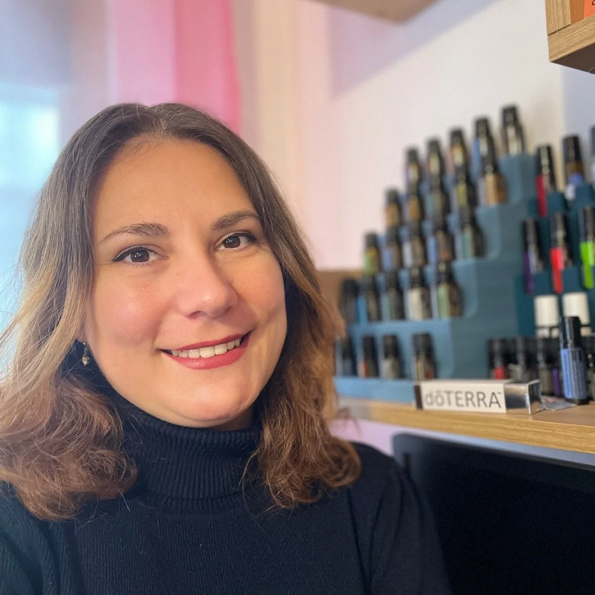 Elena Ouatu-Sarghe, zertifizierte doTERRA Wellness-Beraterin in Schlehdorf, lächelnd vor einem Display mit reinen ätherischen Ölen.