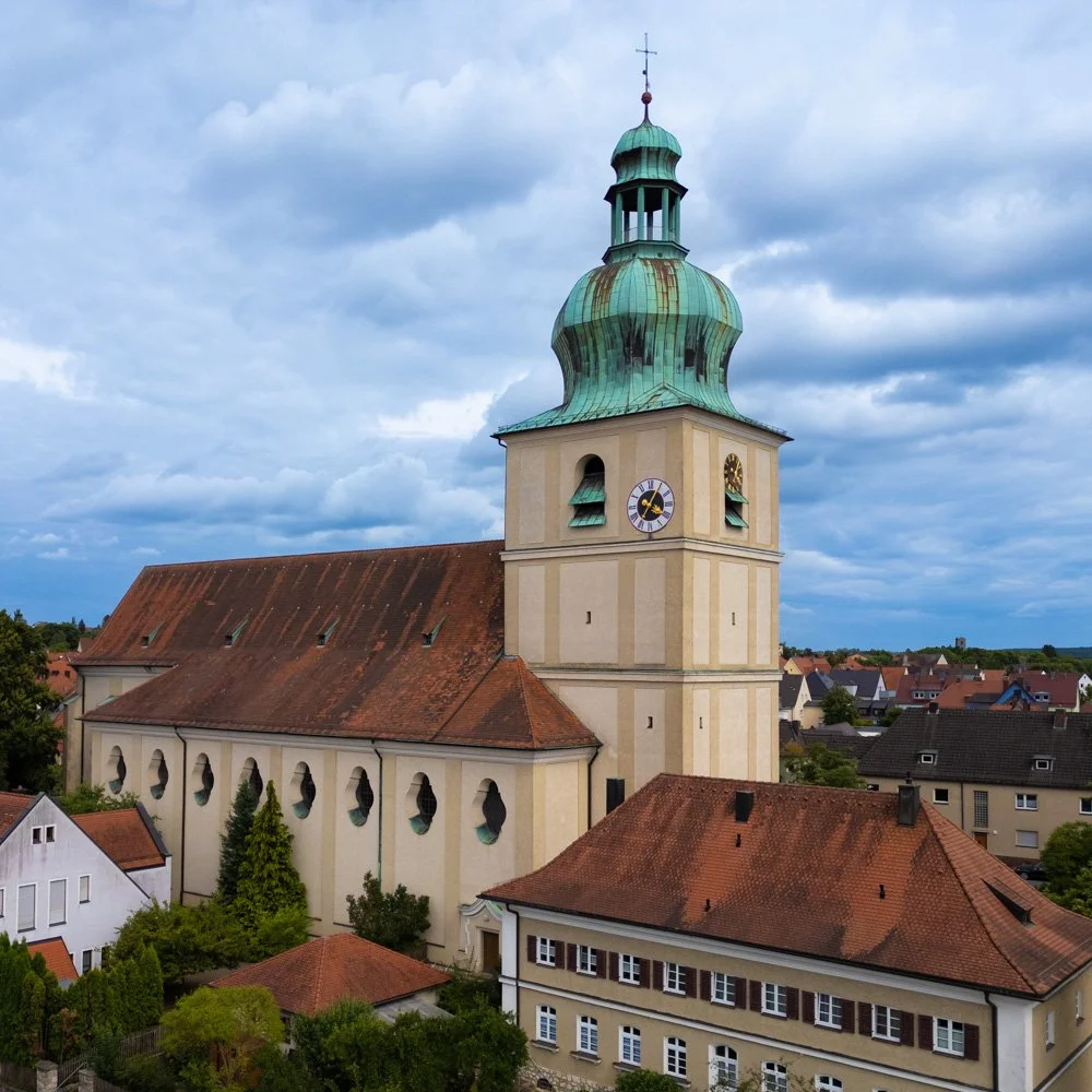 Historische Kirche mit grünem Dach und großem Turm in einer kleinen Stadt bei bewölktem Himmel.