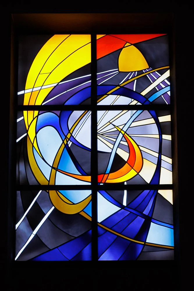 Farbiges abstraktes Glasfenster mit gelben, blauen, roten, schwarzen und weißen geometrischen Formen und Linien.