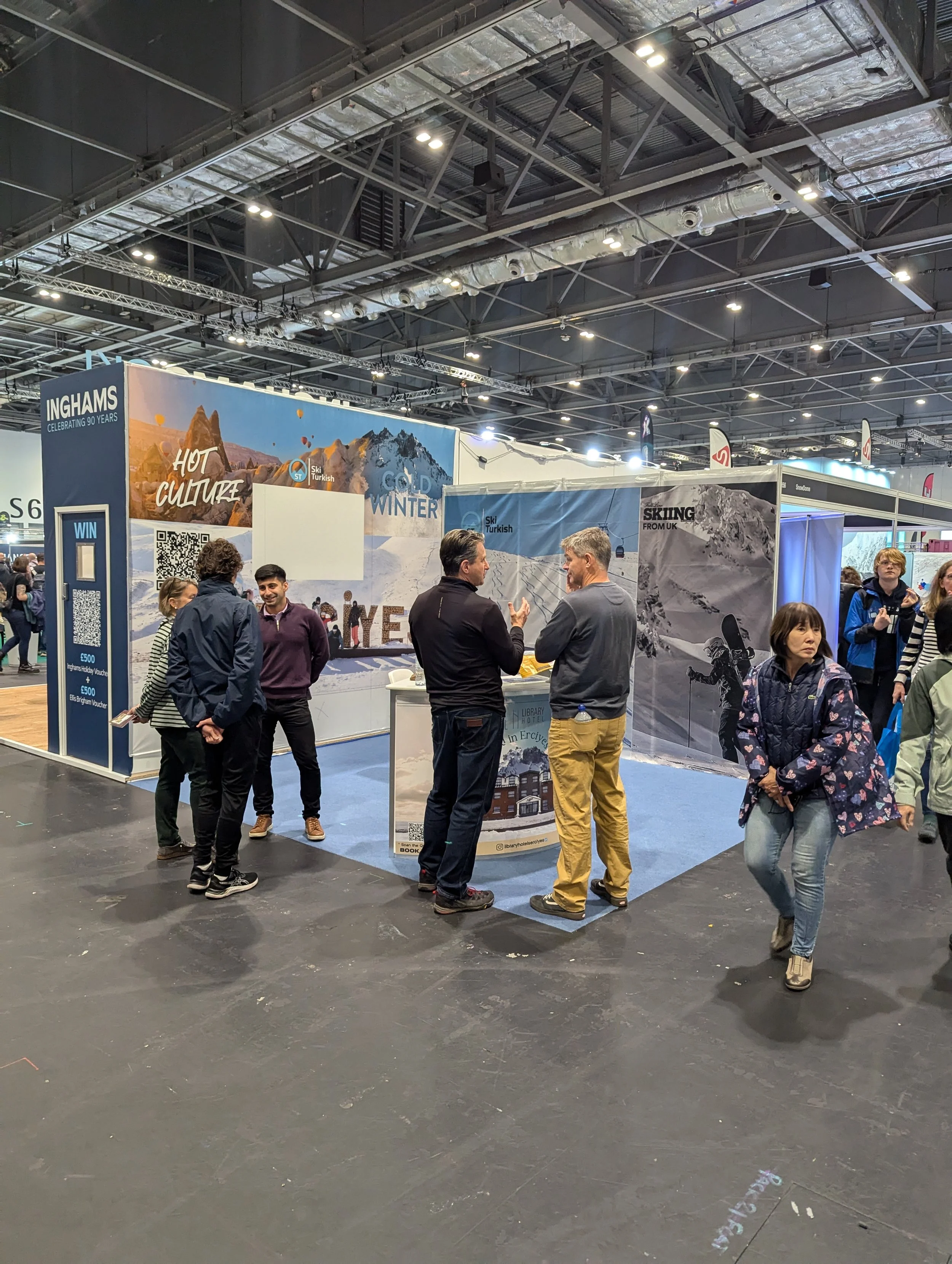 People at a trade show booth promoting winter and ski travel to Turkey, with banners reading 'Hot Culture' and 'Cold Winter,' inside an exhibition hall with high ceilings and bright lighting.