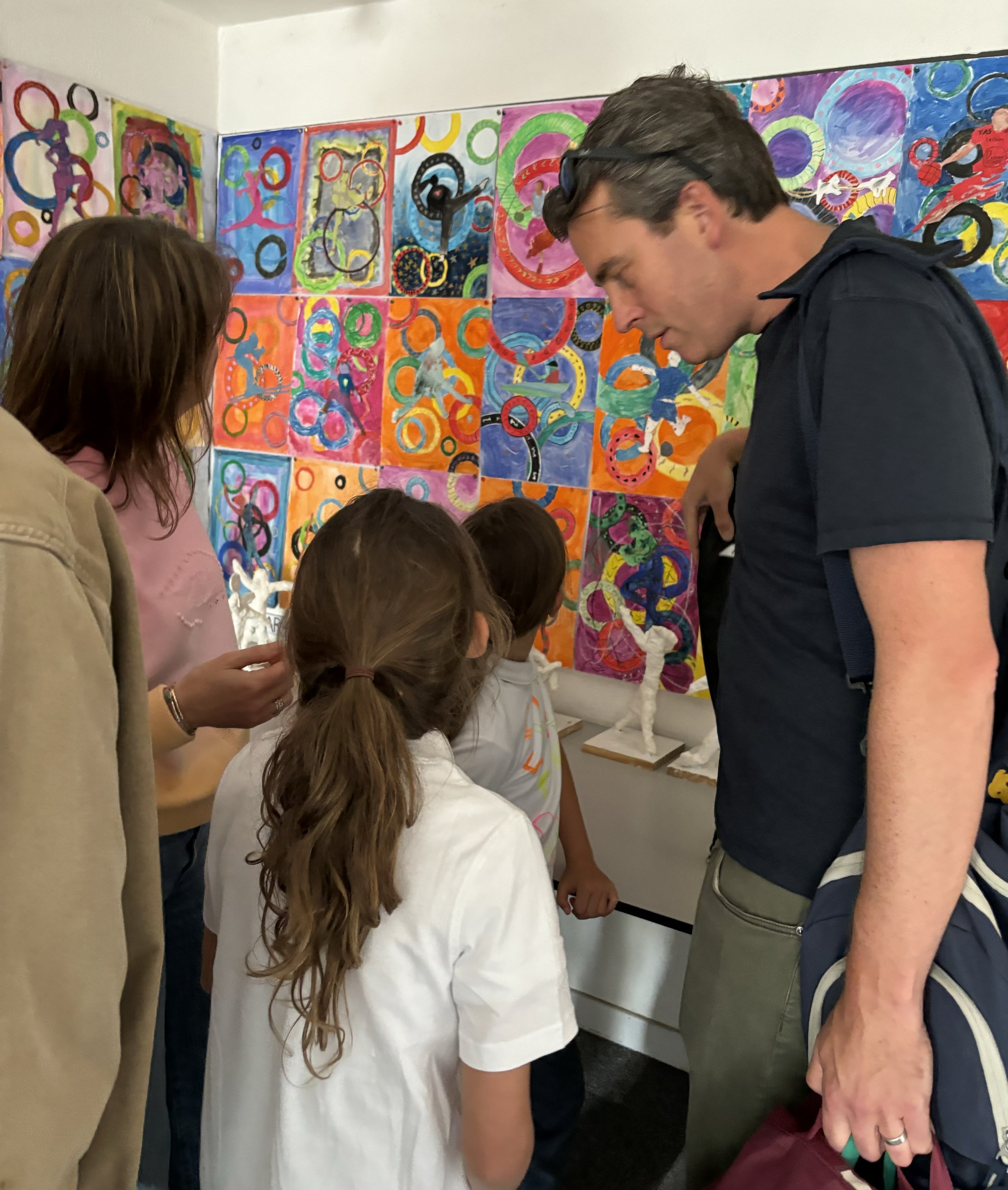 A group of children and adults viewing colorful abstract artwork and sculptures in an art gallery.
