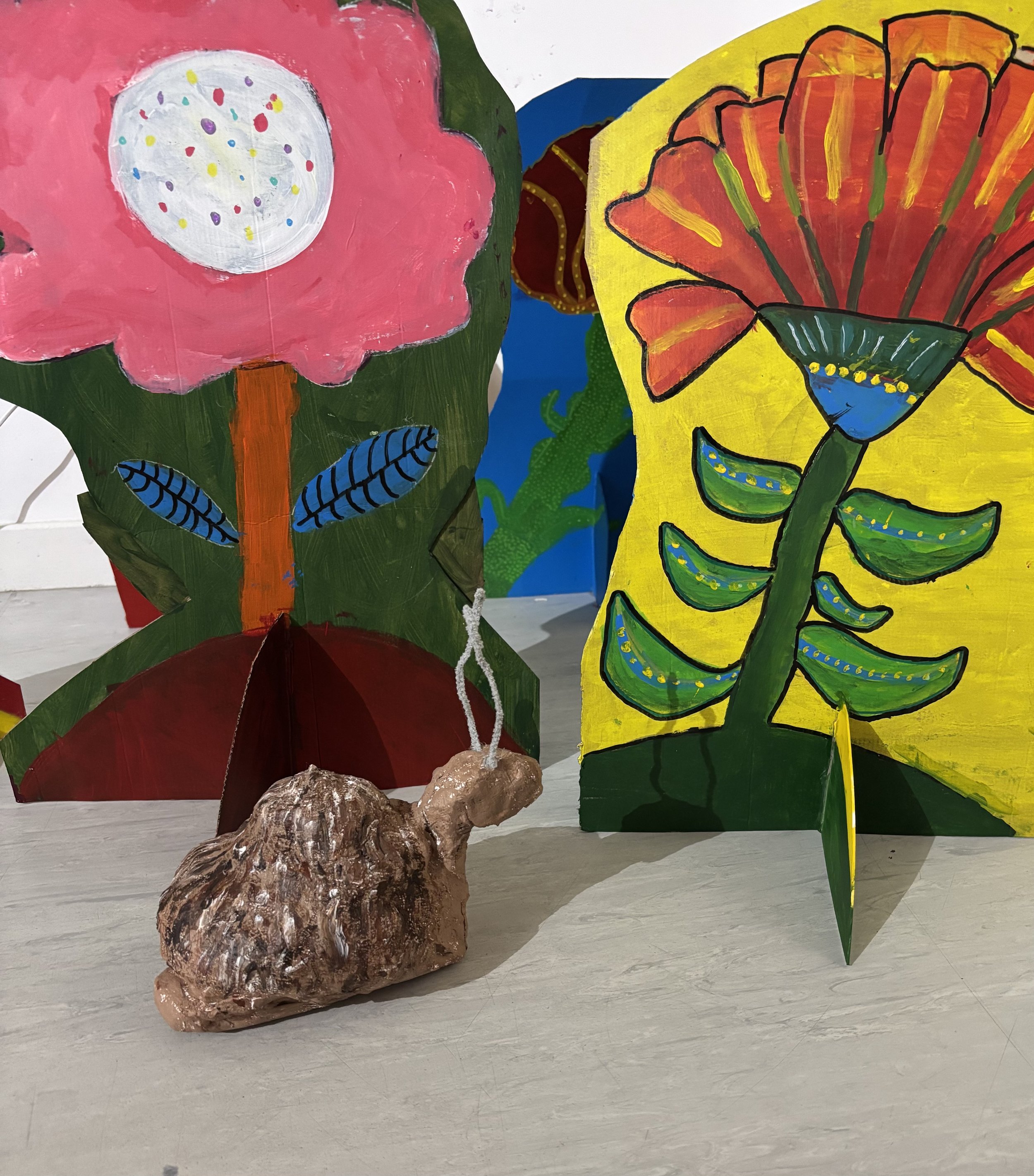 Colorful painted paper flowers on display, with a small, brown, textured sculpture of a rabbit in front.