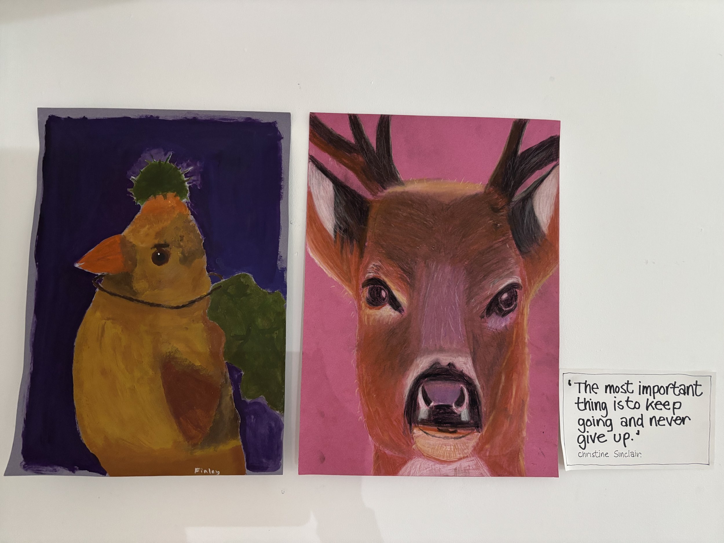 Two colourful paintings of animals are displayed on a wall. The left painting depicts a bird and the right a deer. A small note beside the paintings reads: 'The most important thing is to keep going and never give up.'