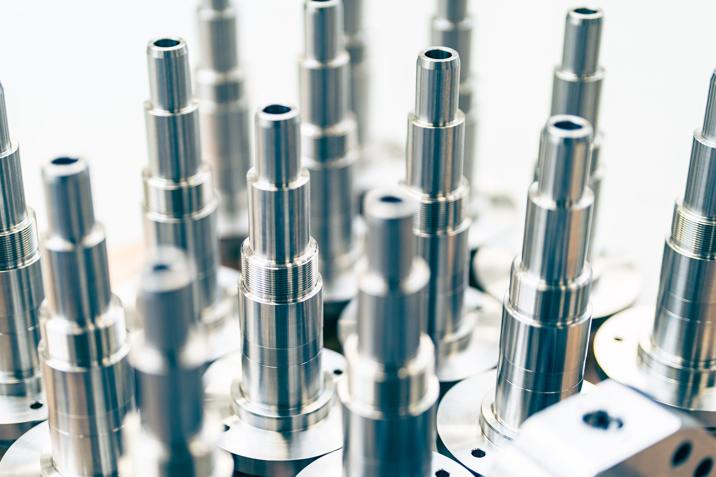 Mann arbeitet mit Kontrollgerät an einer Maschine, hält ein Metallrohr in der Hand, in einer industriellen Umgebung.