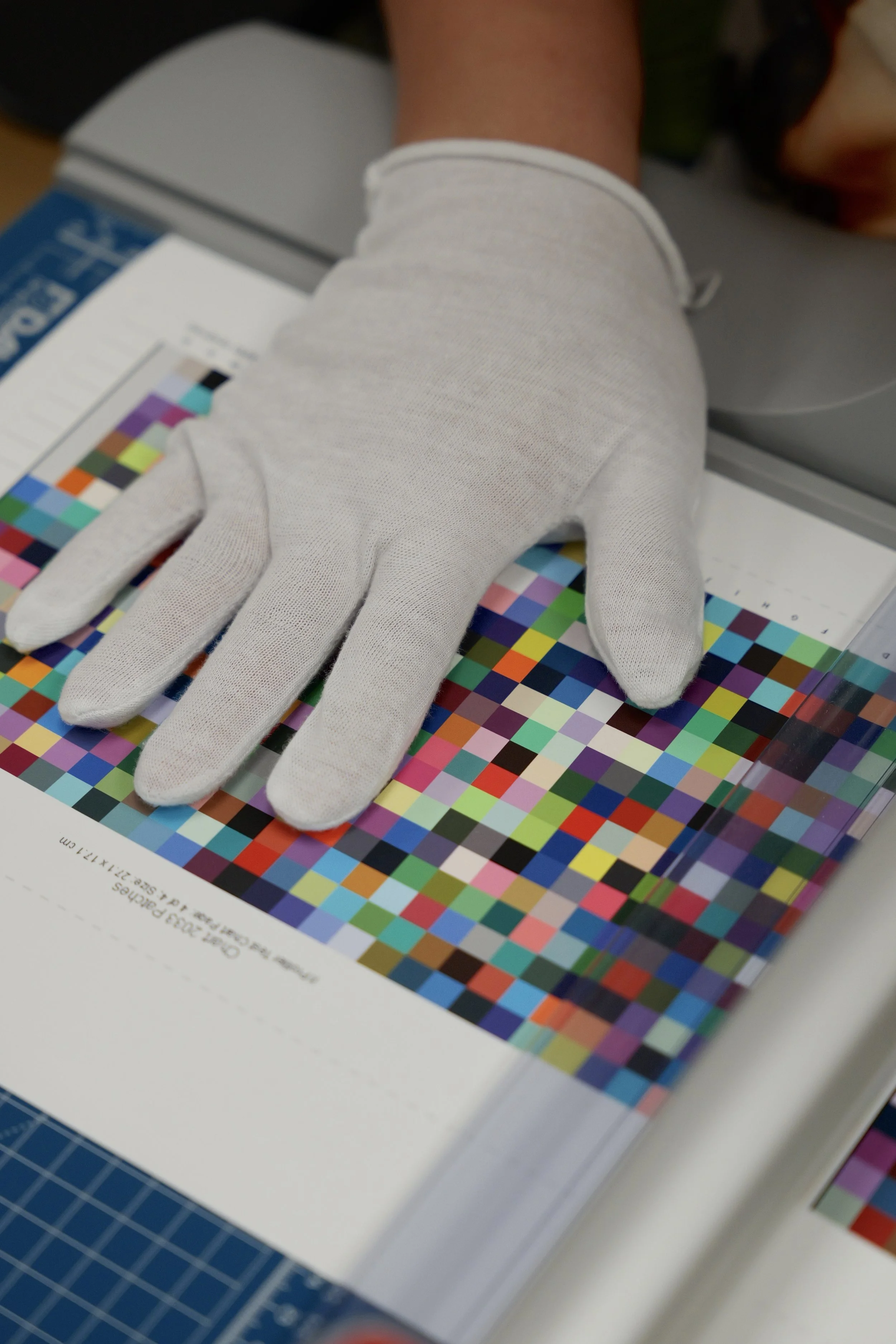 A hand in a white glove resting on a color calibration chart used for printing quality testing.