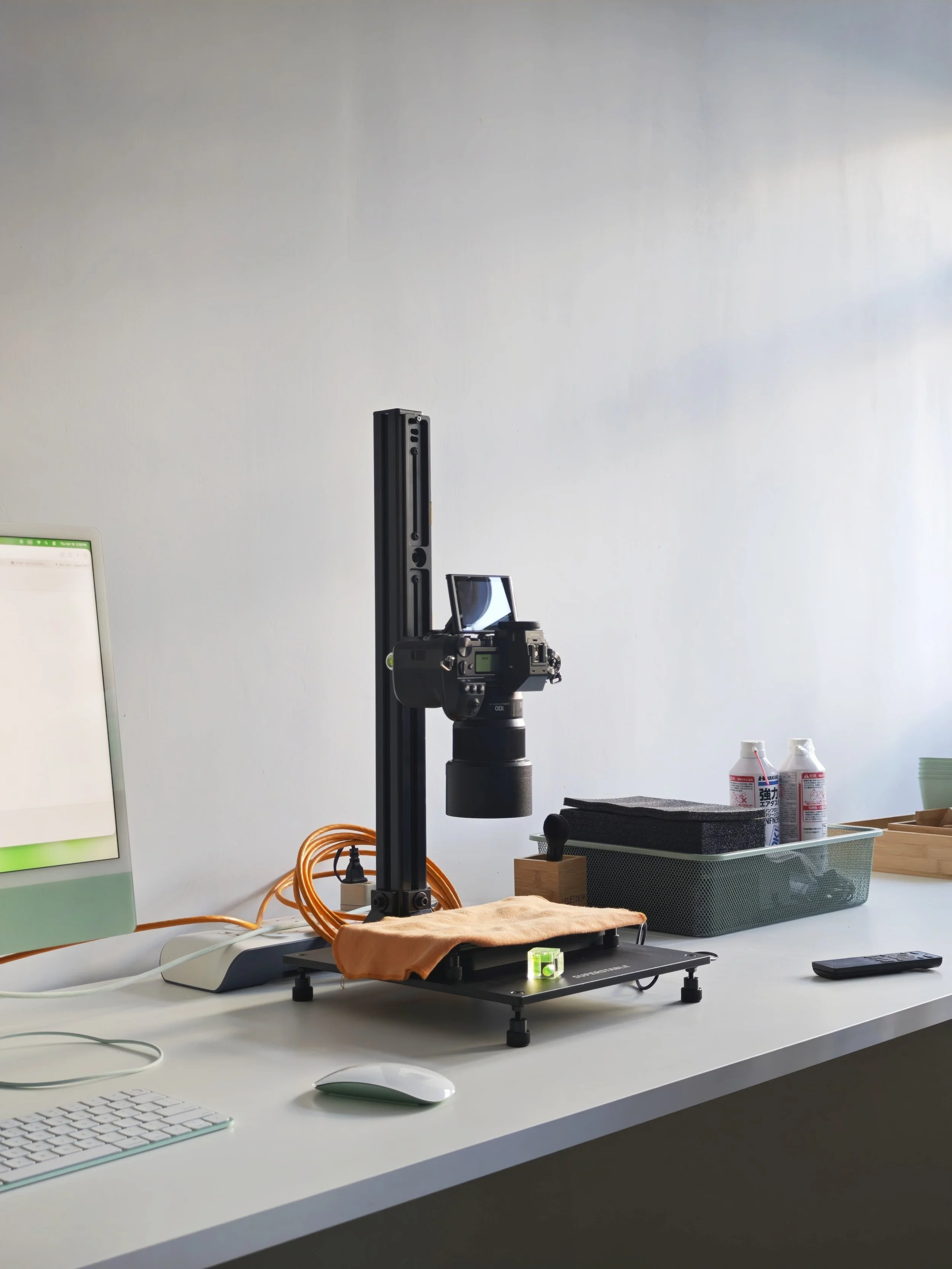 A camera mounted on a stabilizer rig on a desk with a computer monitor, keyboard, mouse, and office supplies in a bright room.