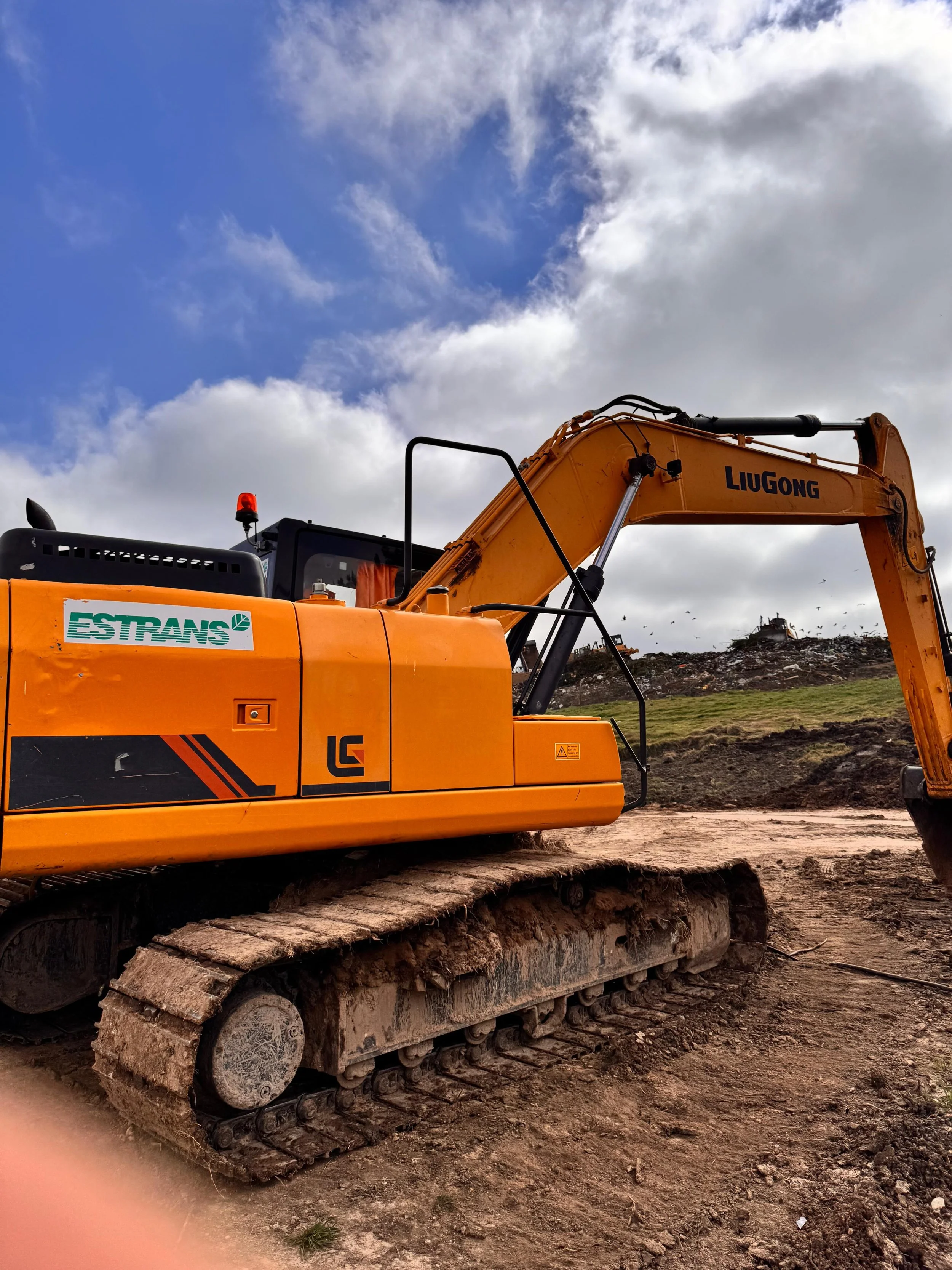 Excavadora naranja en un terreno de construcción con cielo parcialmente nublado.