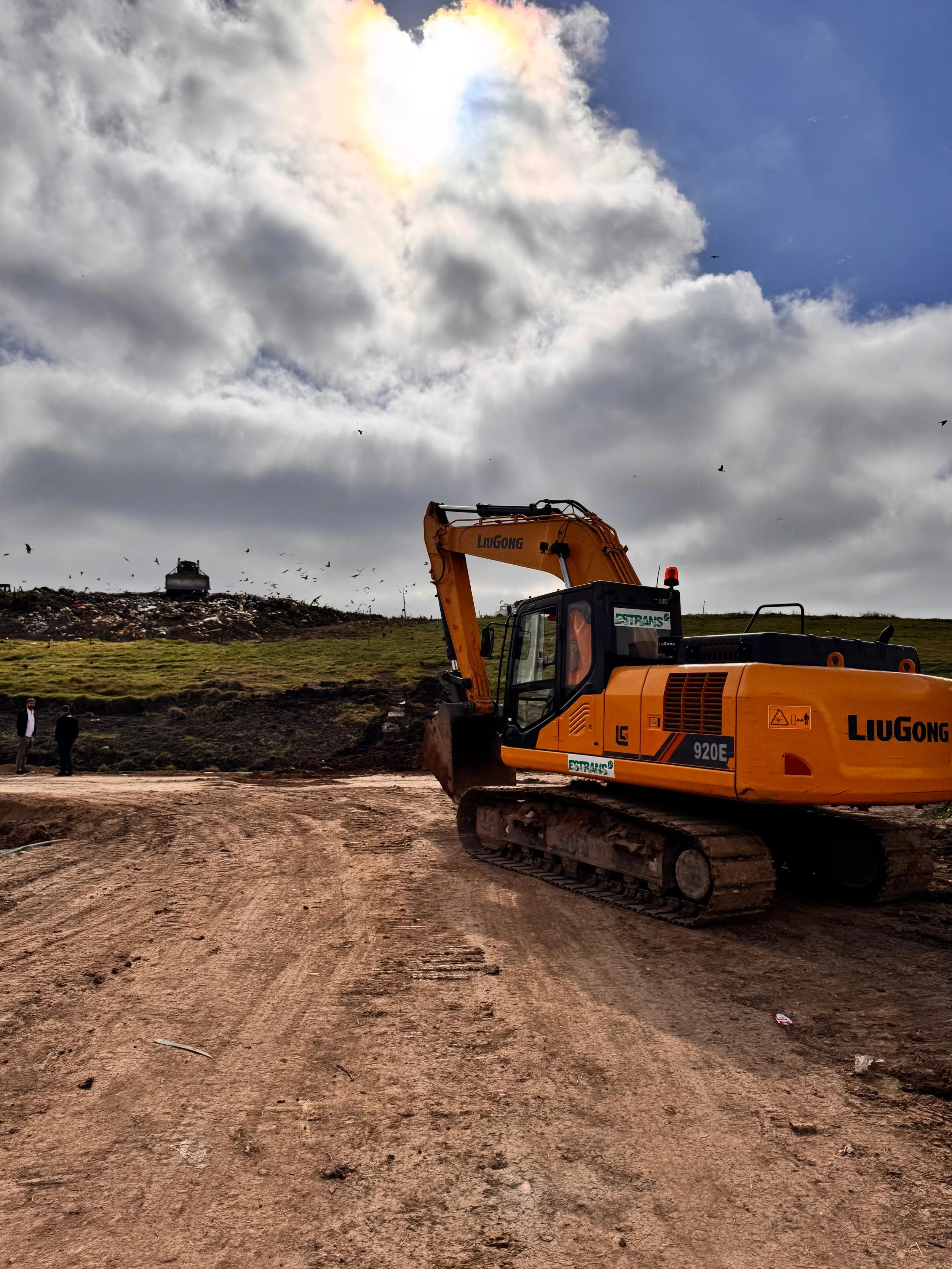 Excavadora amarilla en un sitio de construcción con cielo nublado y aves volando