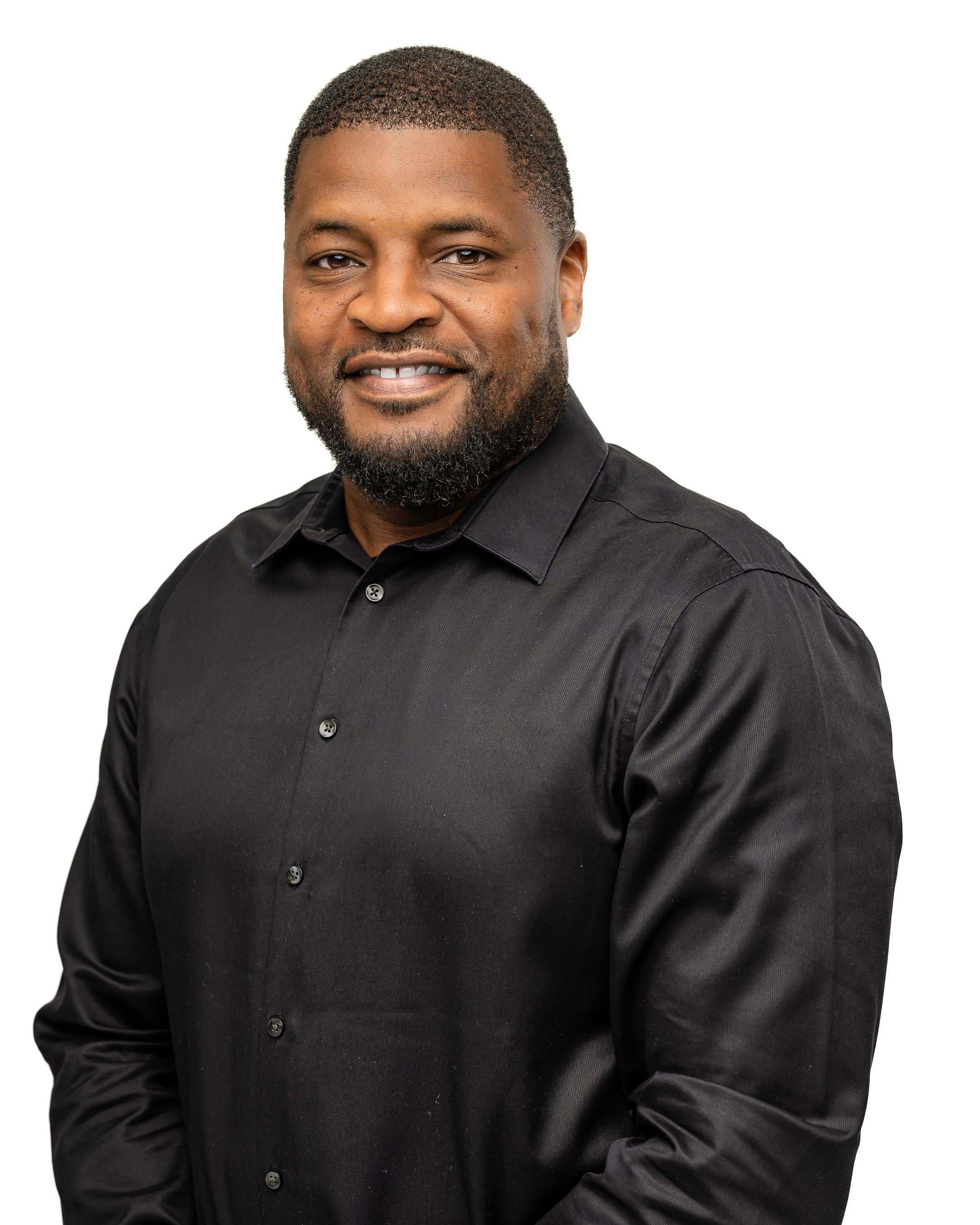 A man with short hair and a beard smiling, wearing a black button-up shirt against a white background.
