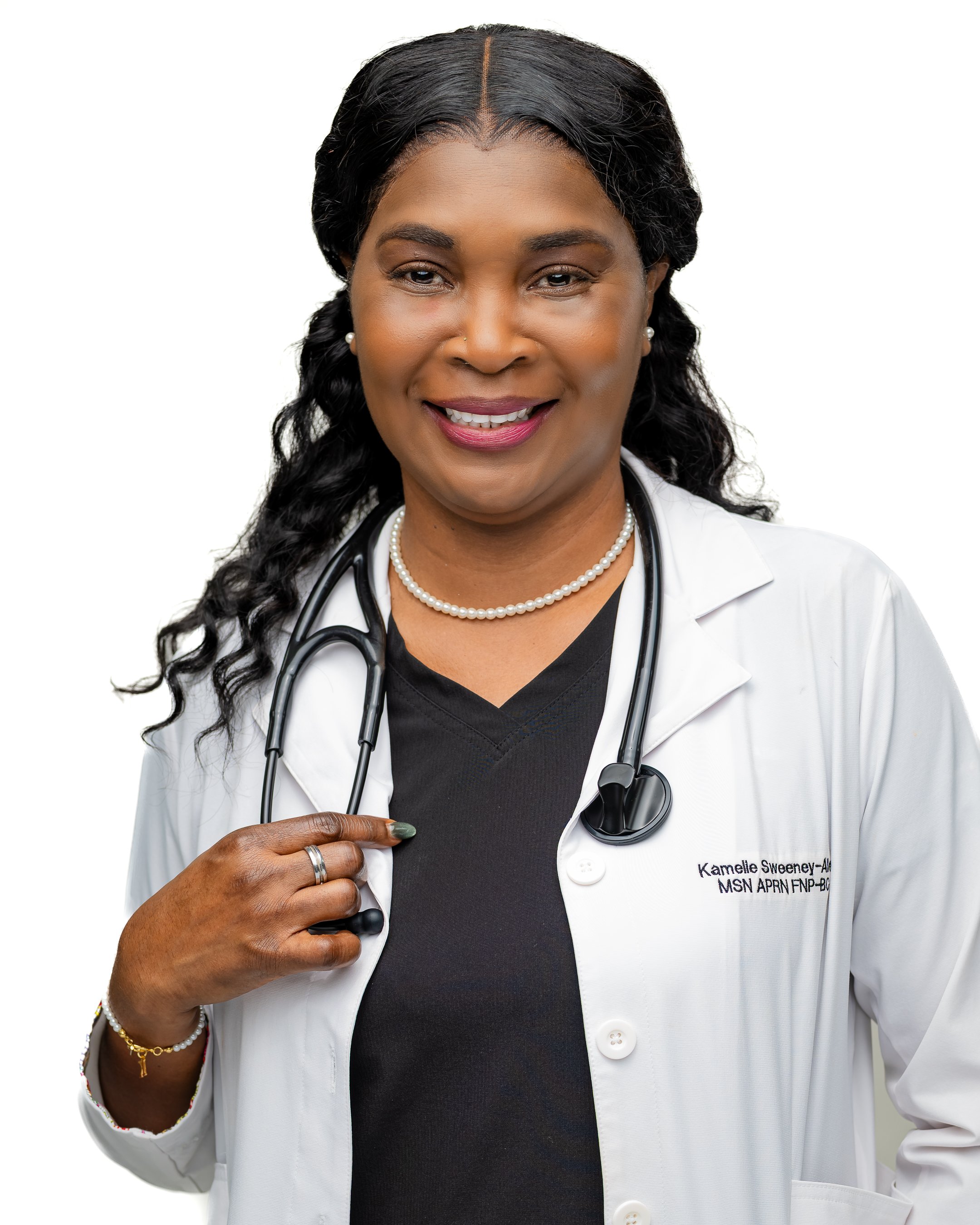 A smiling Black female doctor wearing a white lab coat, black scrubs, and a stethoscope around her neck.