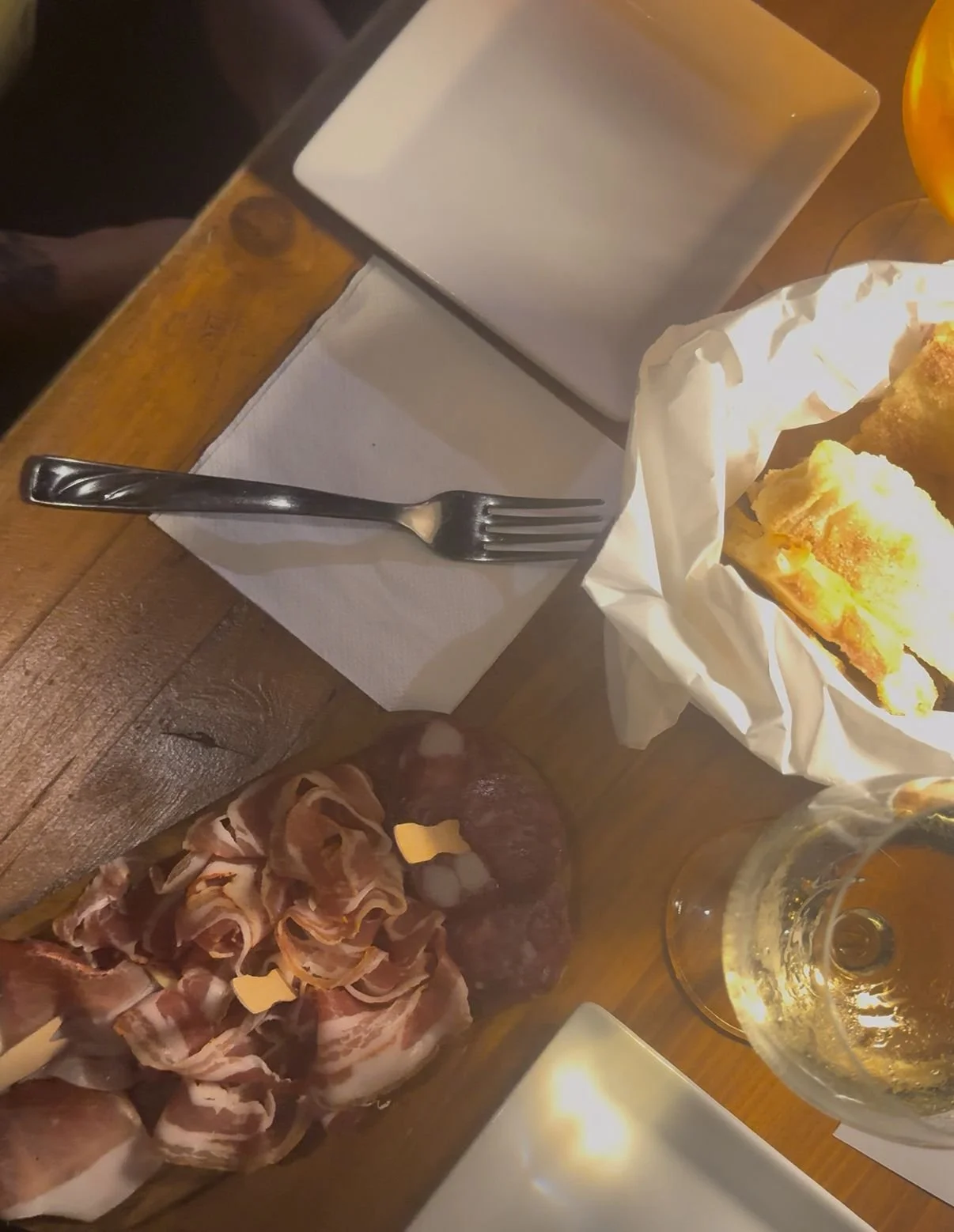 Pane, affettati, bicchiere di birra e piatto con cibo, probabilmente patatine, su una tavola di legno.