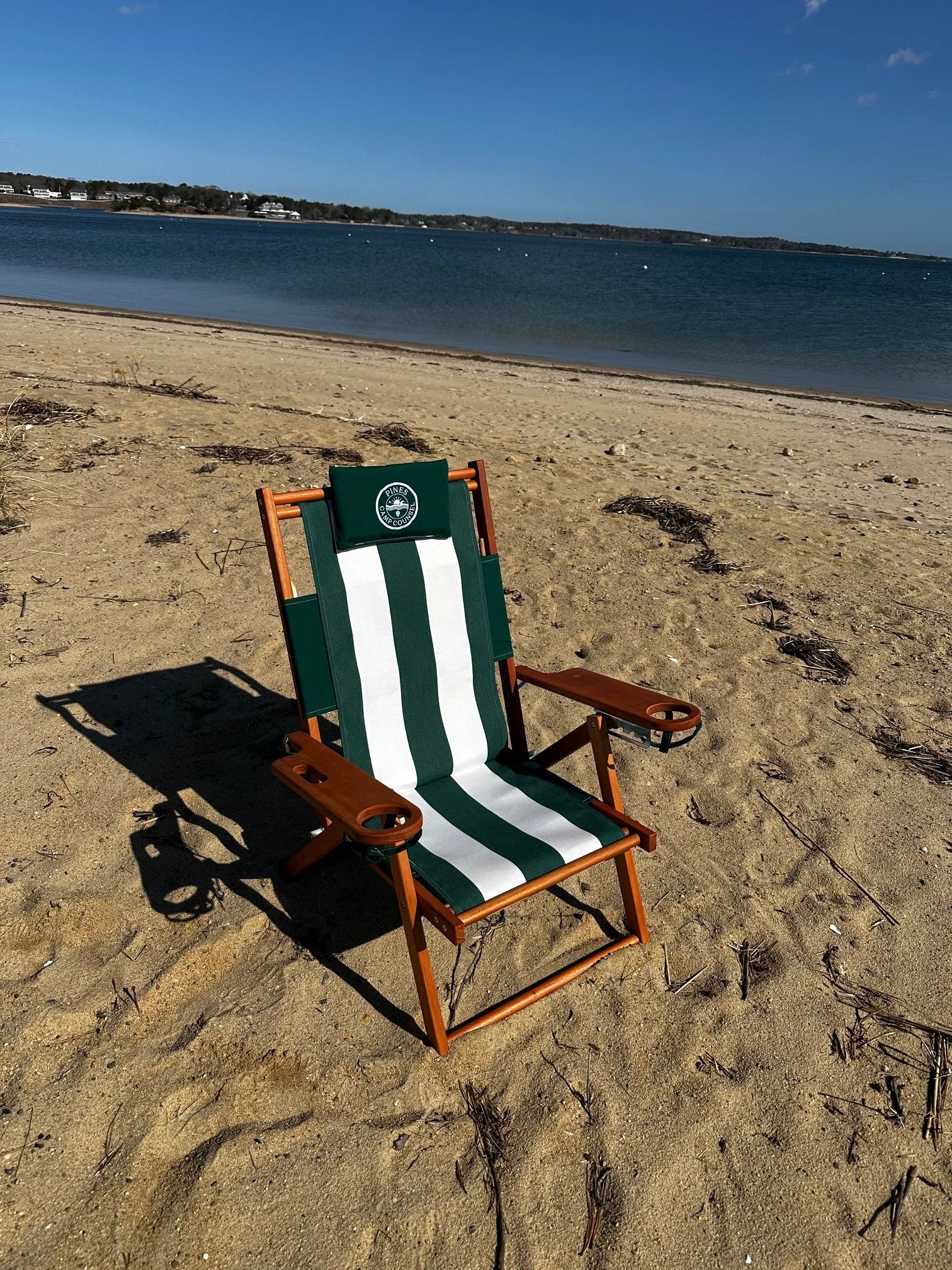 Pines Camp Counsel branded beach chair with green and white stripe and wood frame on sand