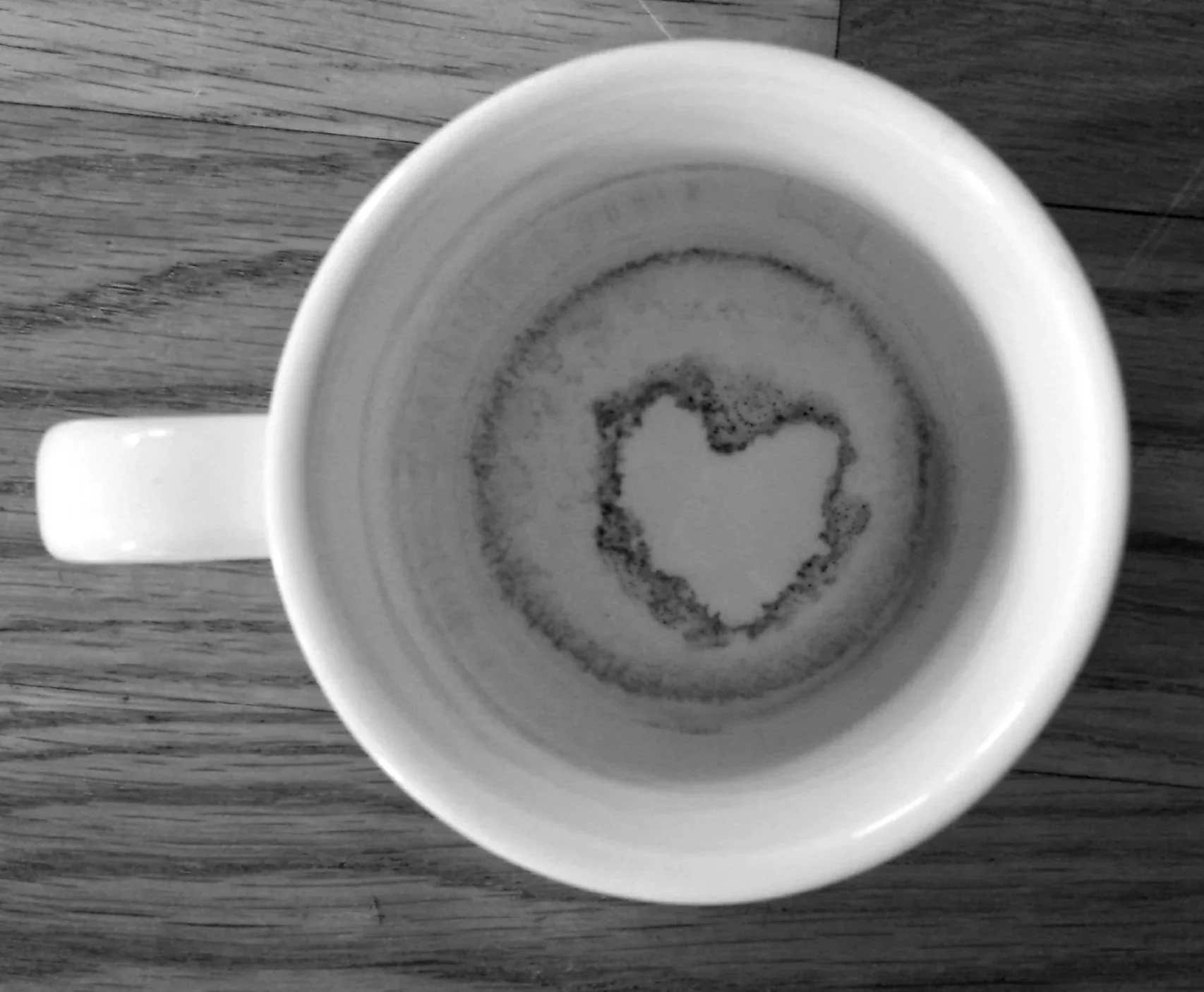 Eine schwarz-weiß-Fotografie, die eine Kaffetasse zeigt, in der sich durch Zufall ein Herz im Kaffeesatz geformt hat.