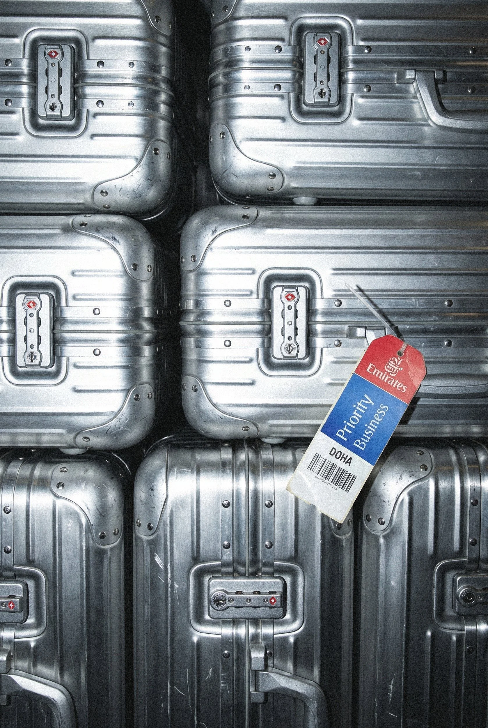 Close-up view of multiple silver aluminum suitcases stacked together, with a Priority Business tag on one of them.
