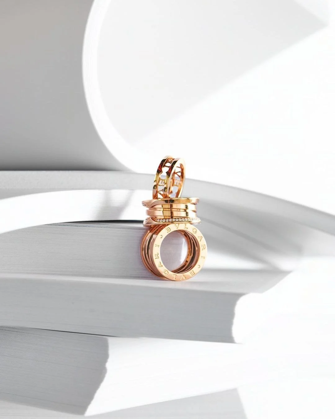 Three gold rings stacked on top of each other, with the top ring featuring cutouts and the middle ring adorned with small diamonds, placed on a white surface with white abstract background.