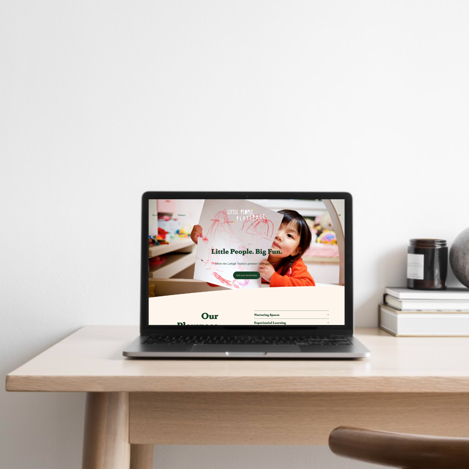 Laptop on a wooden desk displaying a website featuring a young girl holding a drawing, with trees and books nearby.
