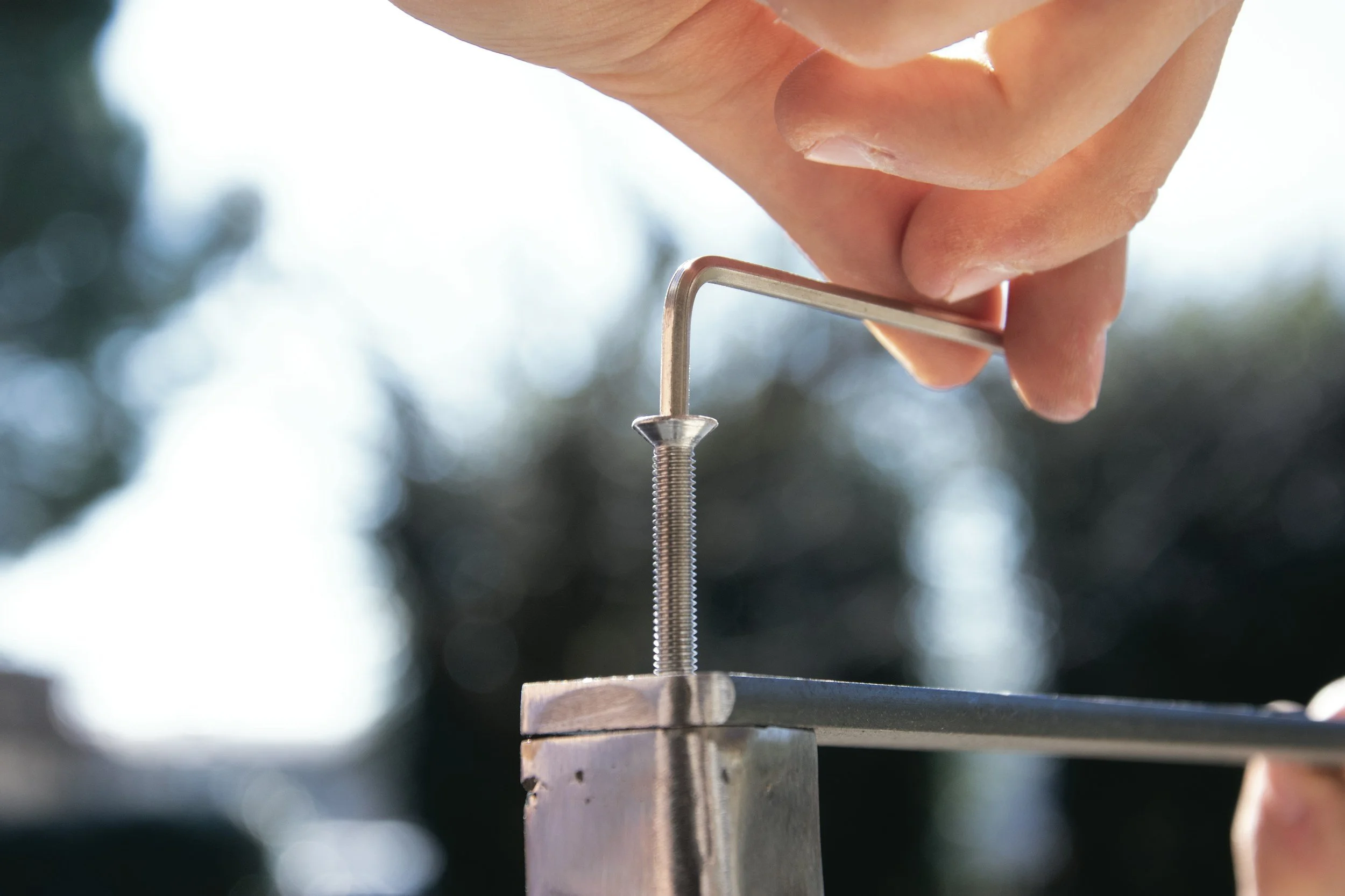 Close-up of a person using an Allen wrench to tighten a screw in metal equipment outdoors.
