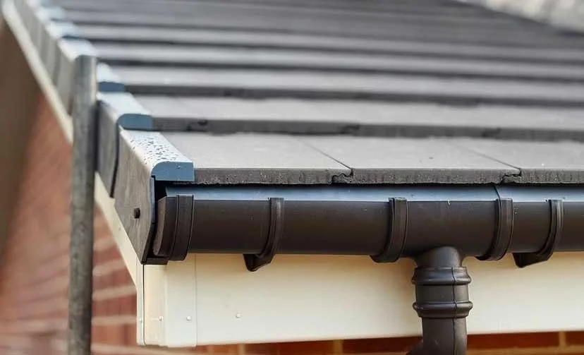 Close-up of the edge of a house roof showing shingles, gutters, and downspout.