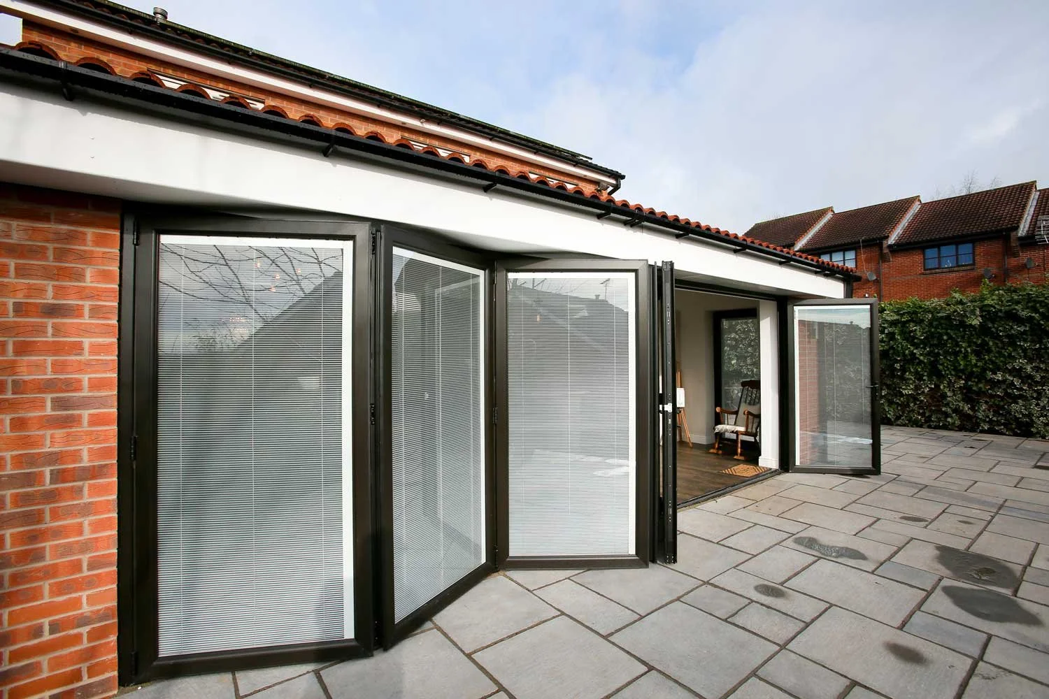Outdoor patio with large black-framed bi-folding glass doors and garden hedge in the background.