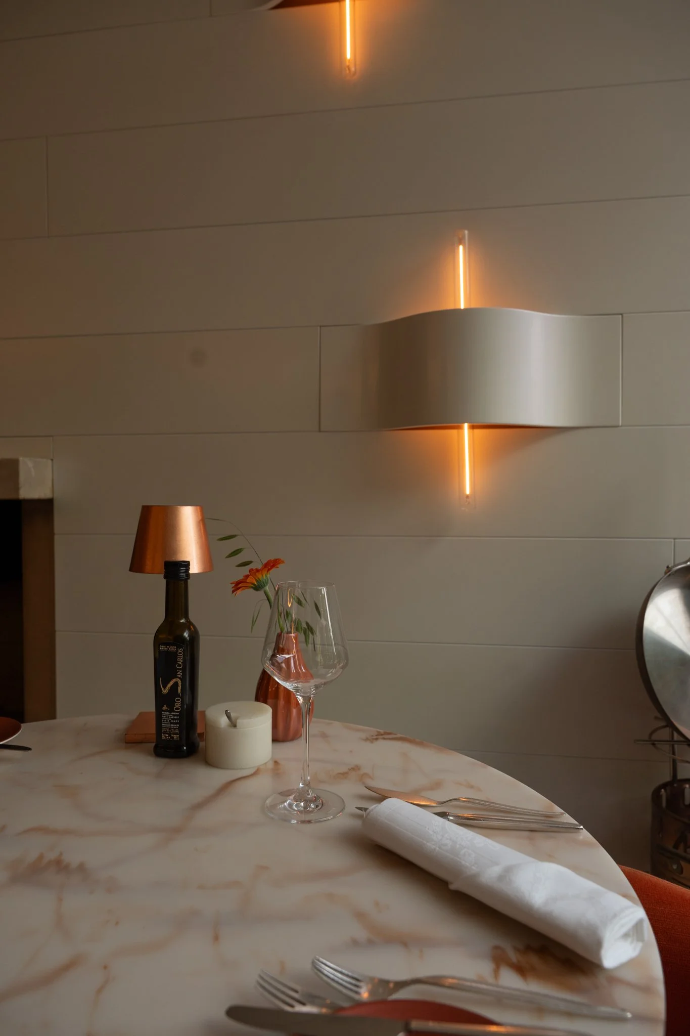 Een buffettafel met een wit marmeren tafel, een wit servet, bestek, een tomatenoranje vaas met een bloem, een wijnglas, een kleine lamp op een fles, een kaars, Brasserie De Bron, Landgoed Groot Warnsborn Arnhem