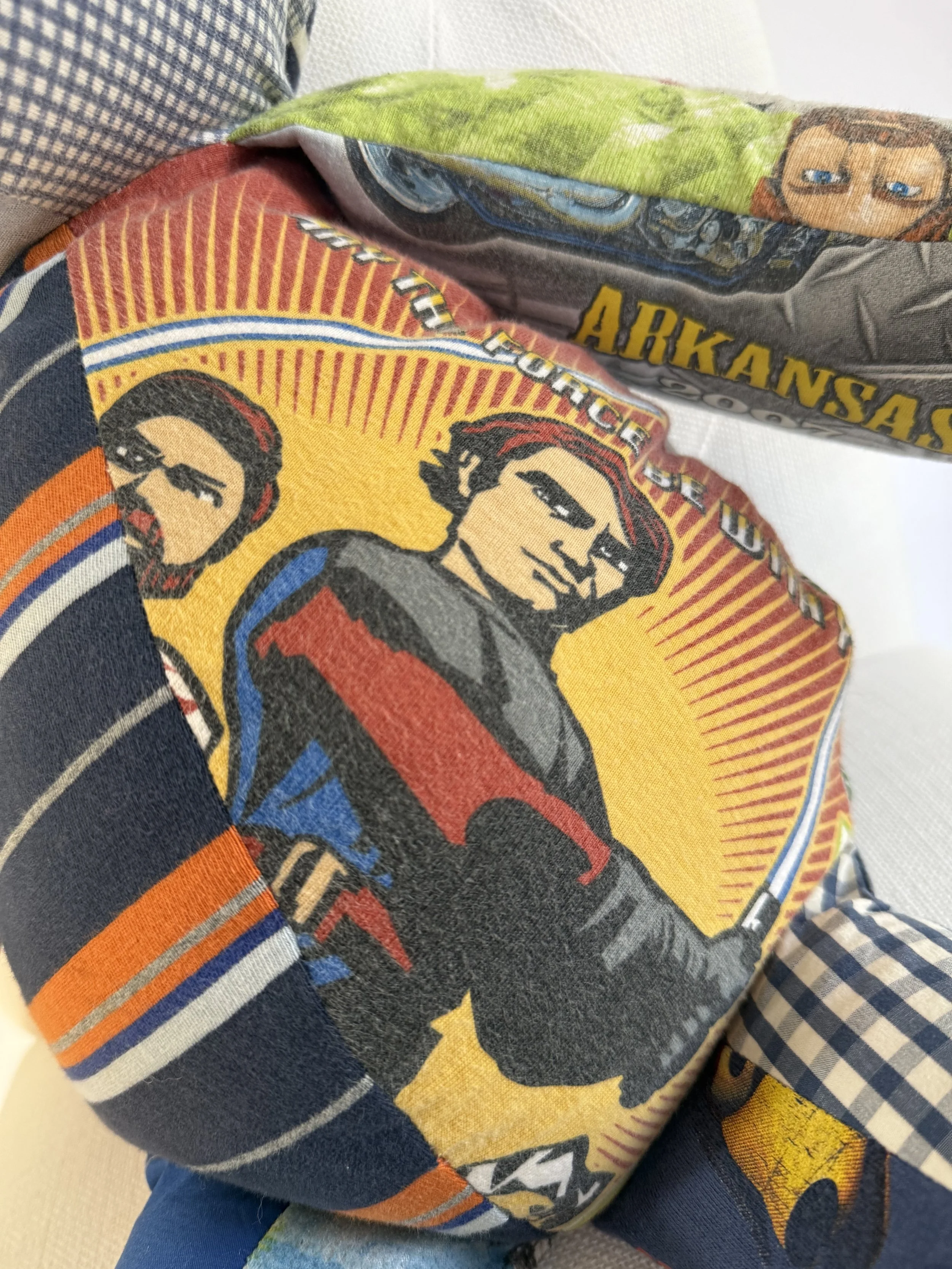 Close-up of a quilted fabric featuring a comic-style illustration of two men with a yellow background and red lines. The fabric includes parts of text and other patterns, with additional fabric pieces around.