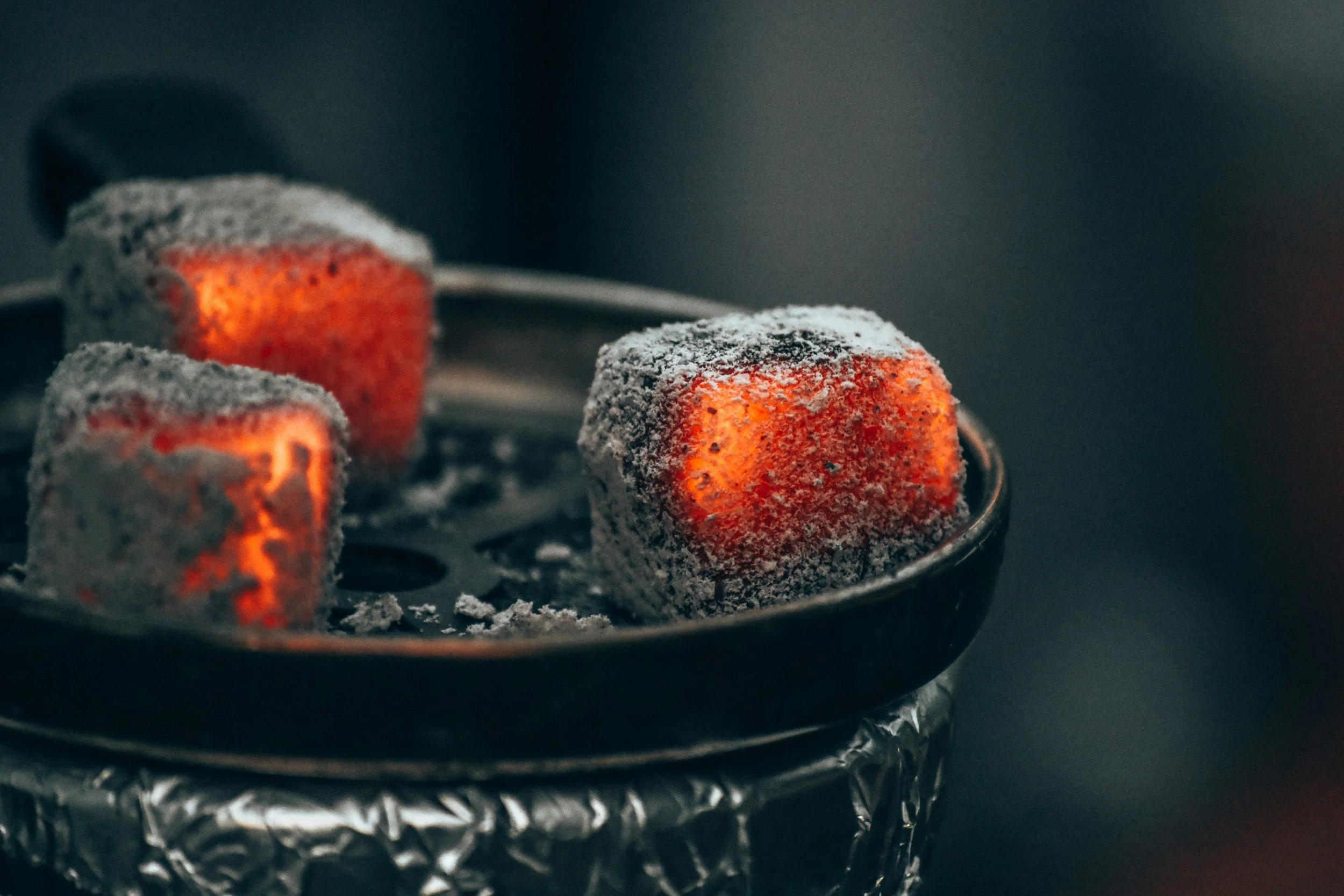 Hot charcoal briquettes with glowing red centers and a layer of ash on top inside a metal container.