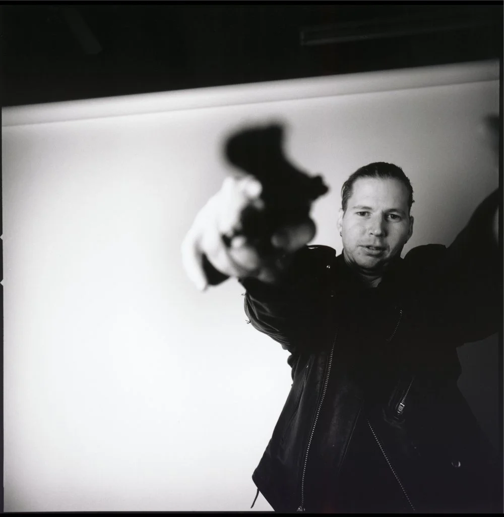 A person pointing a gun at the camera in a black and white photo. Created by Sam Devine Tischler © all rights reserved