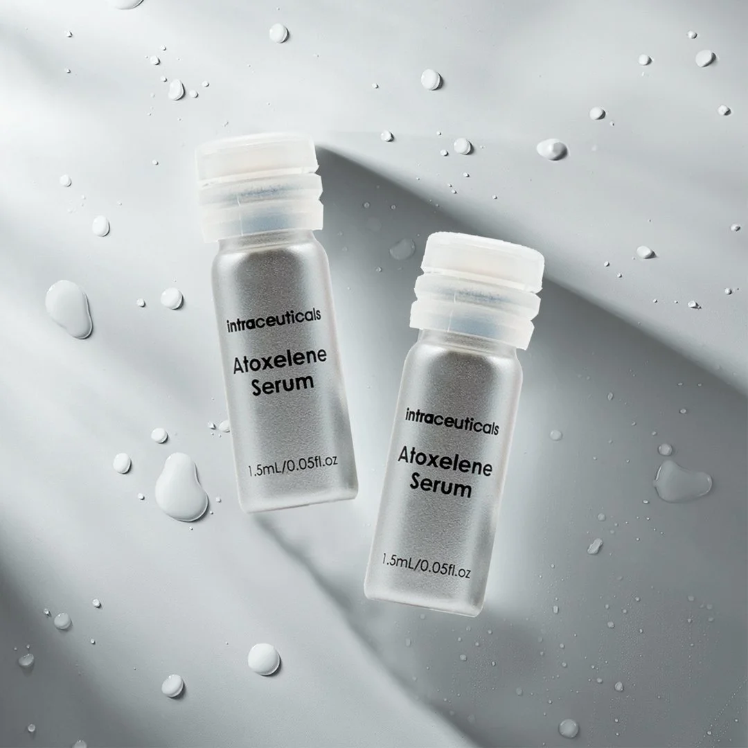 Two bottles of Intraceuticals Atoxelene Serum with water droplets and splashes on a white surface.
