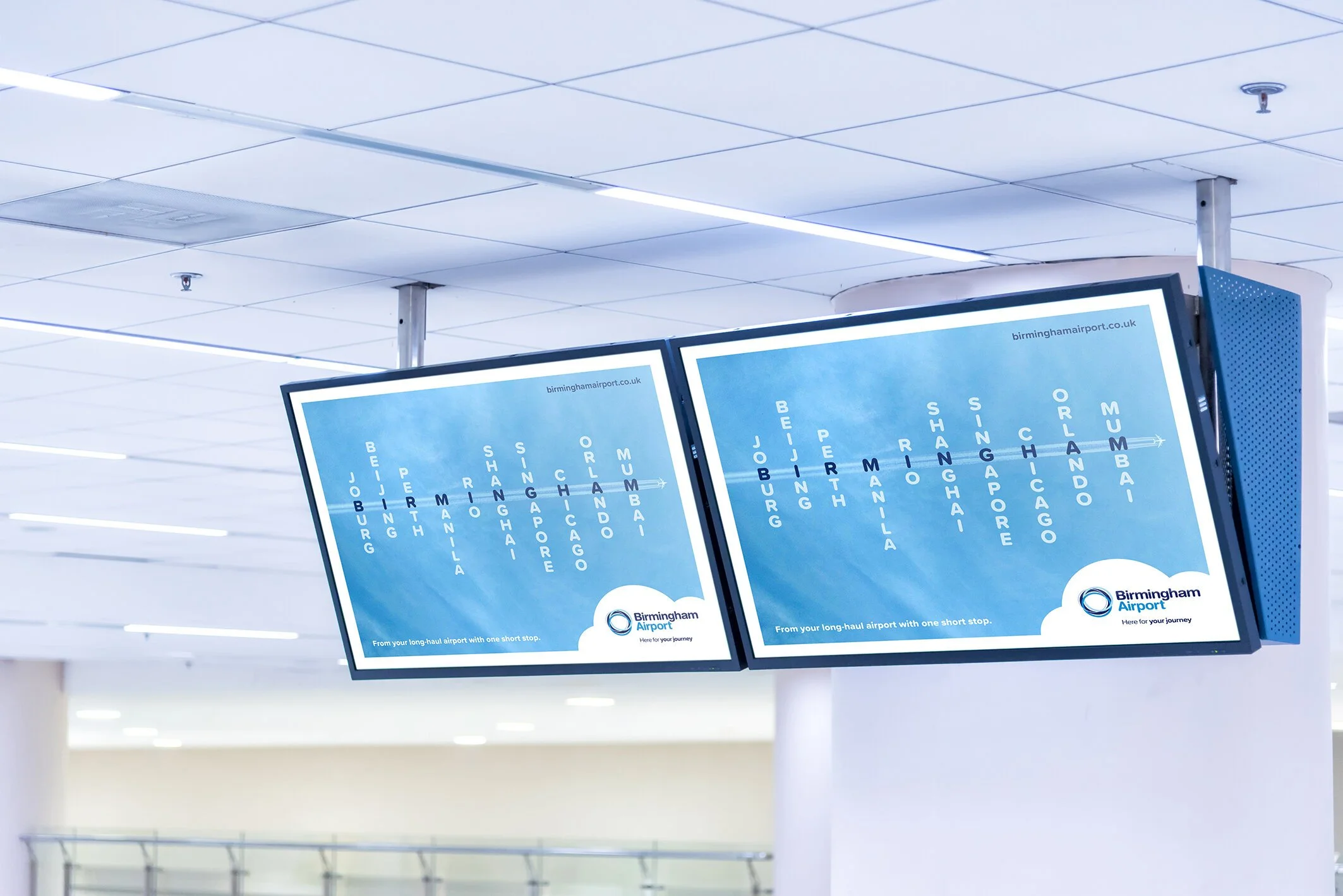 Two digital flight information screens at Birmingham Airport displaying flight destinations in blue with white text, showing departures to Johannesburg, Beijing, Manila, Singapore, Chiang Mai, Hong Kong, Chicagoland, Orlando, and Mumbai.