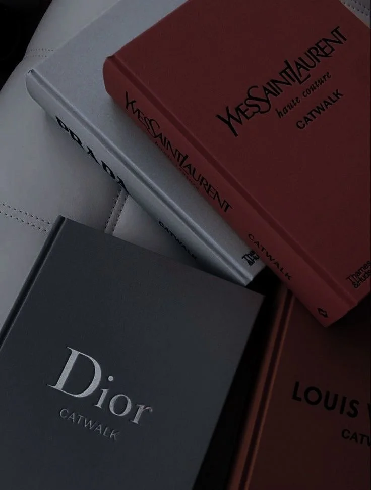 Close-up of three fashion books titled 'Yves Saint Laurent', 'Dior', and 'Louis Vuitton' on a white surface.