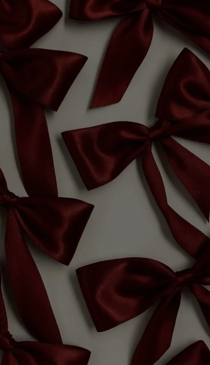 Multiple burgundy satin bows on a white surface.