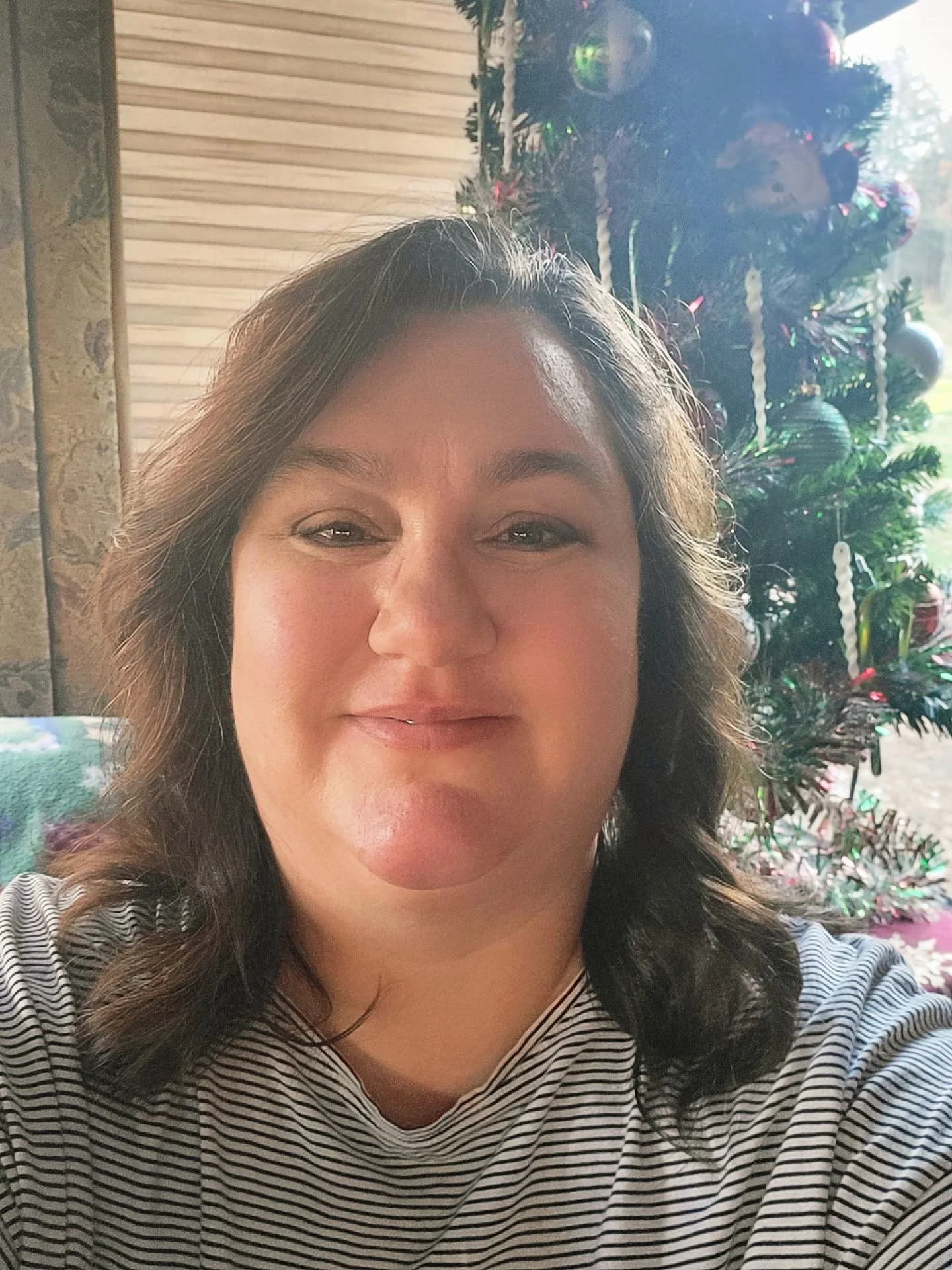 A woman taking a selfie in front of a decorated Christmas tree.