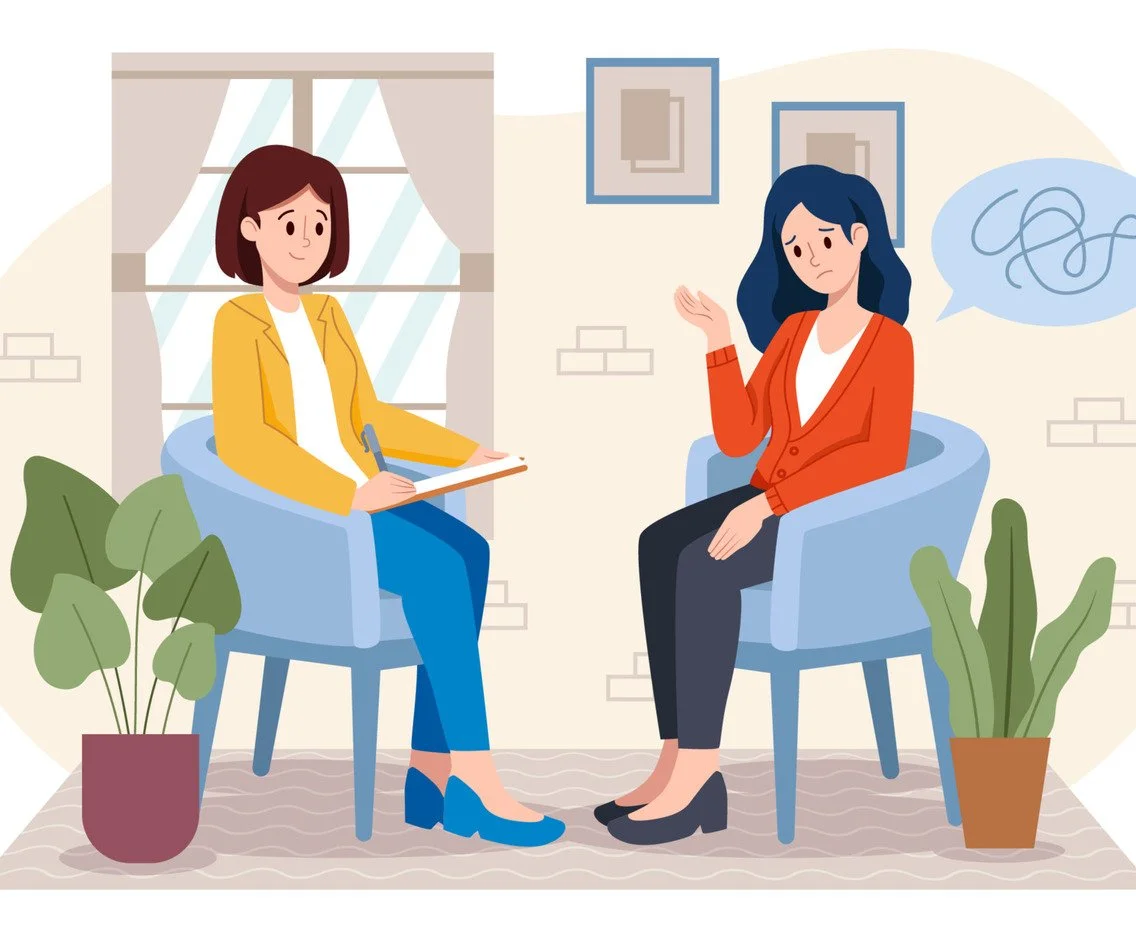 A woman sitting on a blue chair during a therapy session, talking to a therapist who is taking notes, in a cozy room with plants and framed pictures.