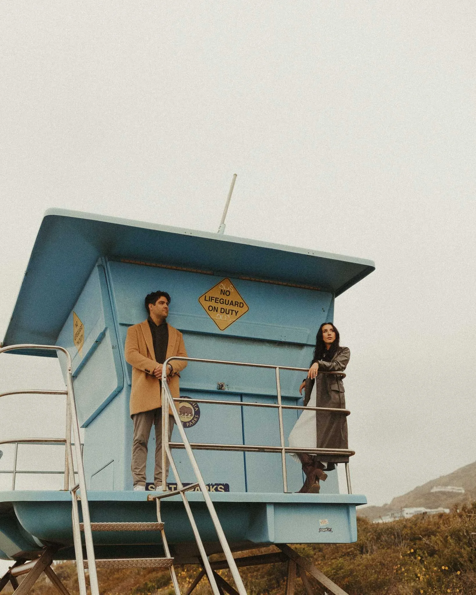 engaged couple standing on lifeguard stand staring into the distance during malibu beach california engagement session