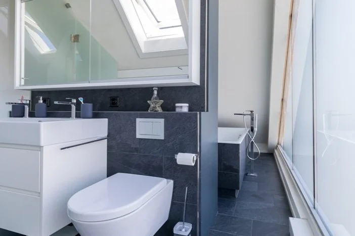 Modernes Badezimmer mit Toilette, Waschbecken, Spiegel, Badewanne, großer Fenster und Dachfenster.
