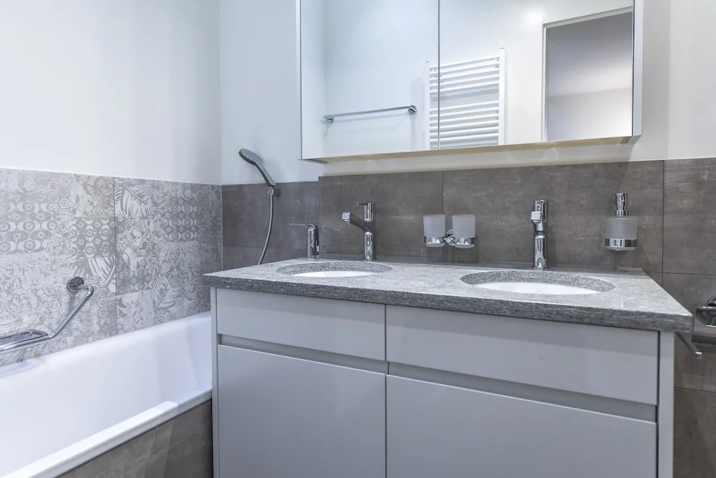 Badezimmer mit Doppelwaschbecken, Spiegel, Handtuchhalter und Badewanne.