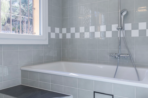 Badezimmer mit Badewanne, grauen Wandfliesen und Fenster.