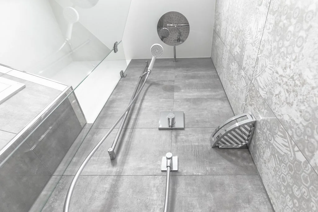 Dusche mit Handbrause, Badewannenhaltegriff, Duschabzieher, Duschkopf, Wasserhahn und einen runden Spiegel an der Wand.