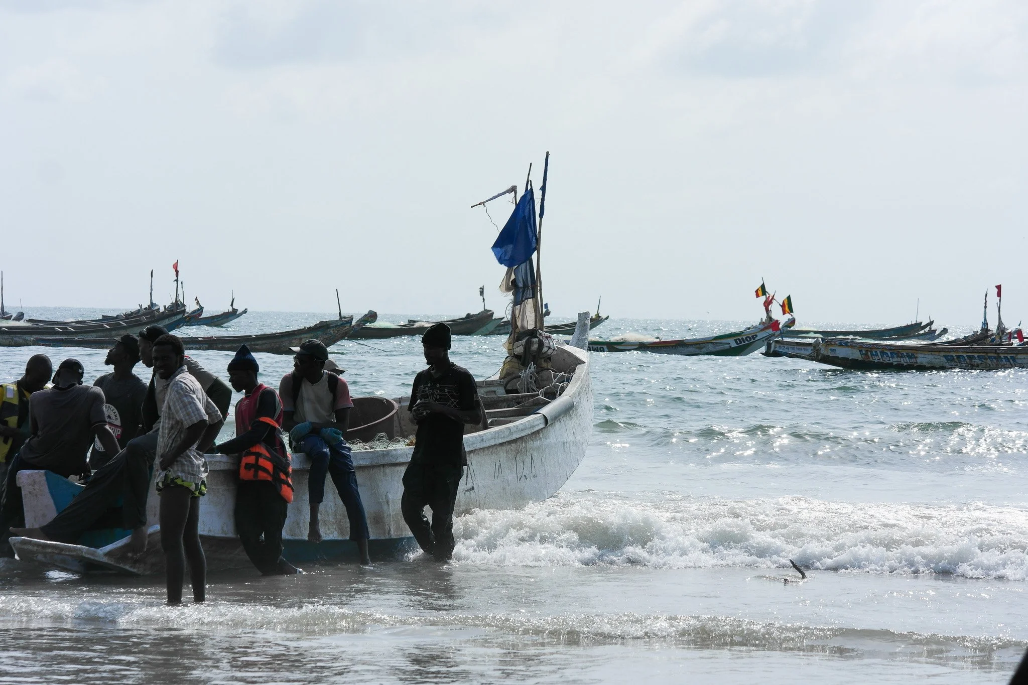 Gens qui sortent un bateau de la mer, plusieurs petits bateaux en arrière-plan, scène en bord de mer par jour ensoleillé.