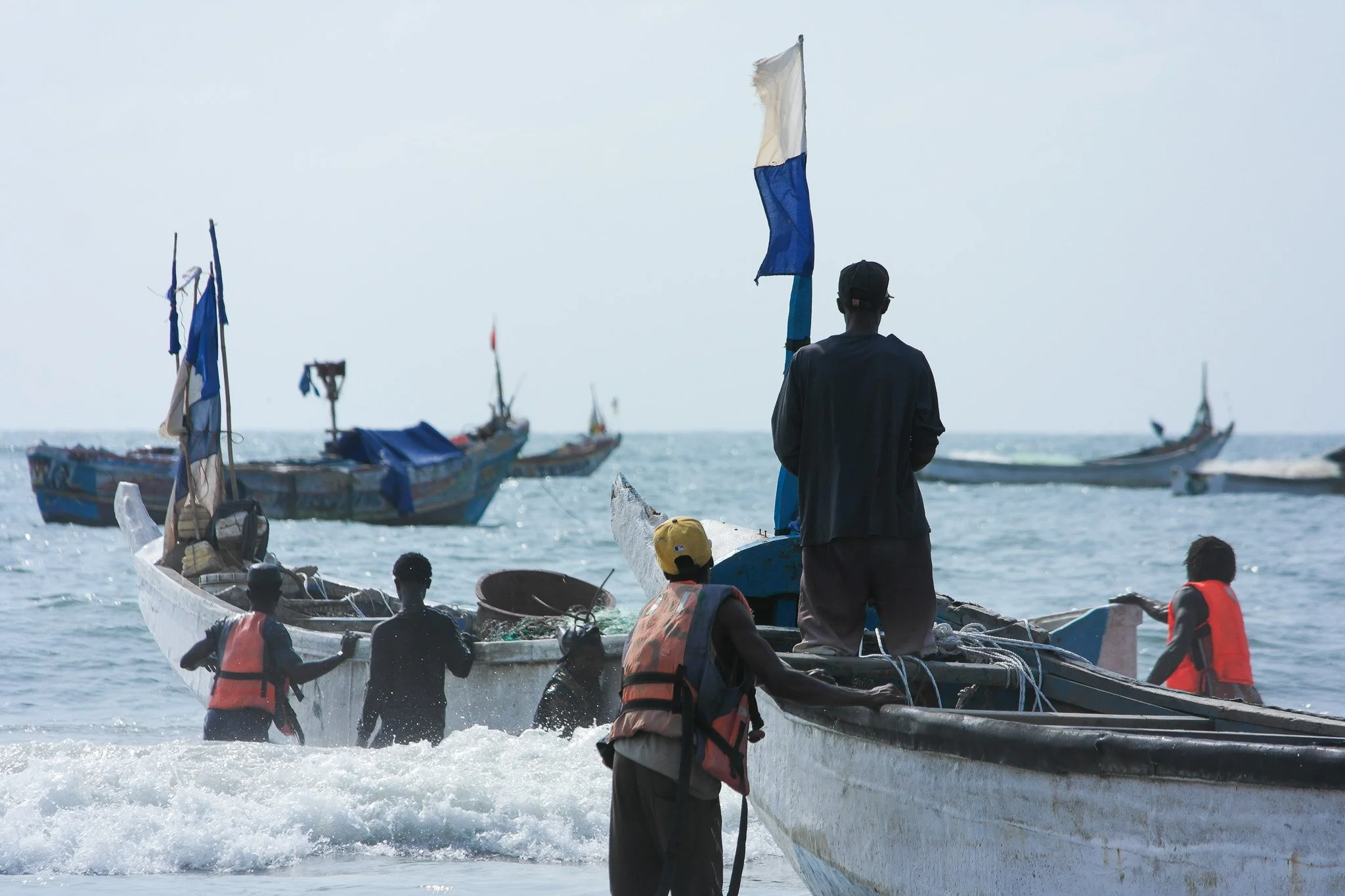 Groupe de personnes avec des gilets de sauvetage à côté de bateaux de pêche en mer.
