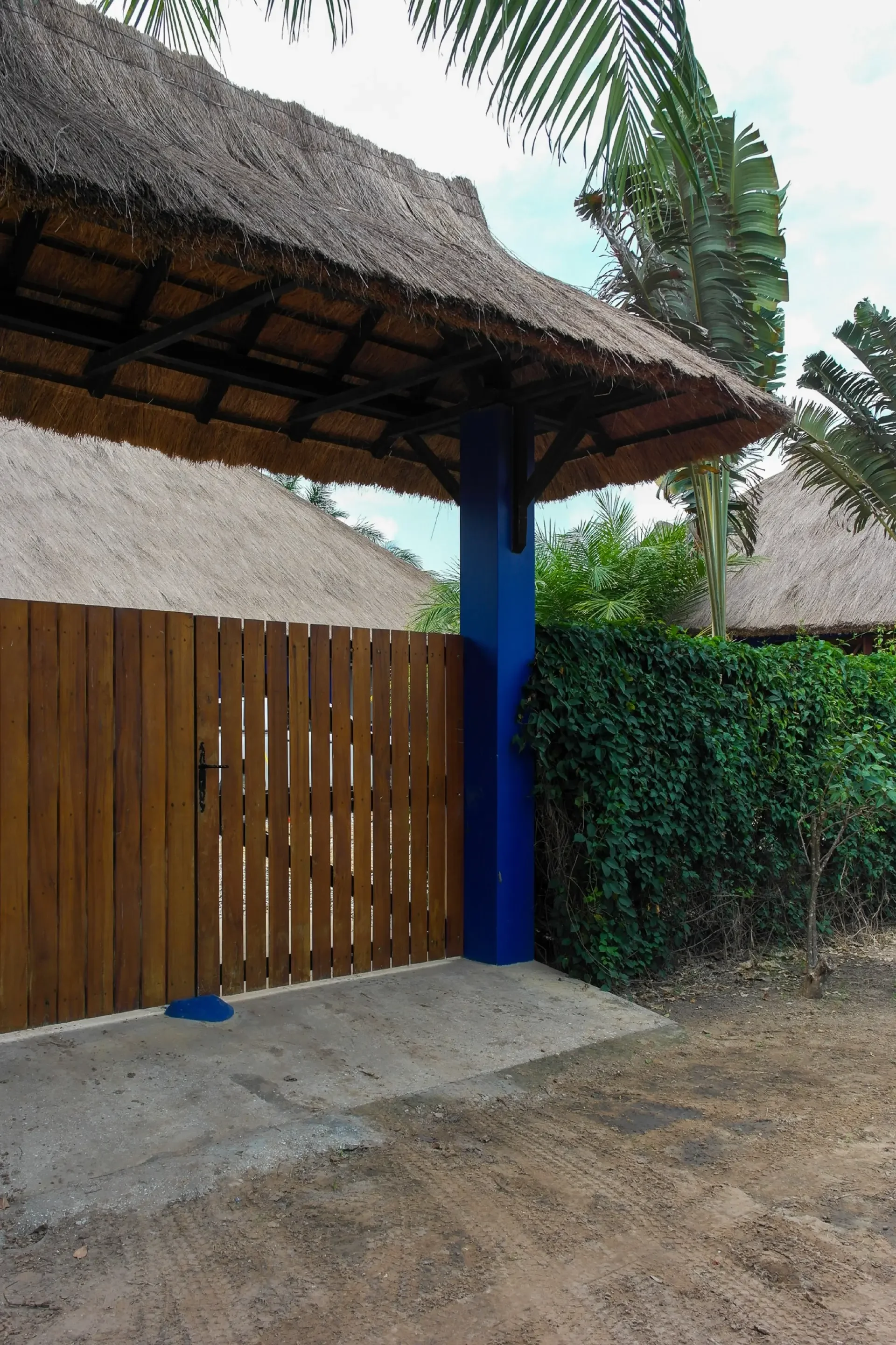 Une porte en bois avec une clôture en bois et un toit en chaume, entourée de végétation tropicale