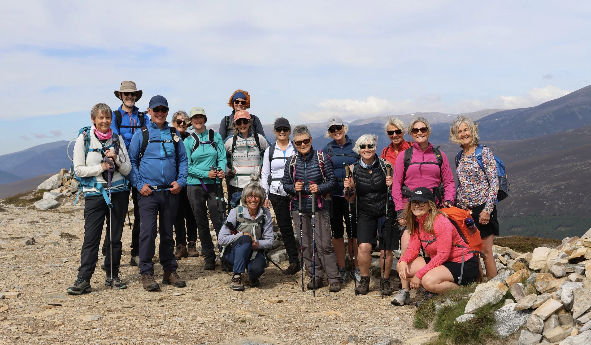 Group of hikers on a mountain trail with mountains and cloudy sky in the background.