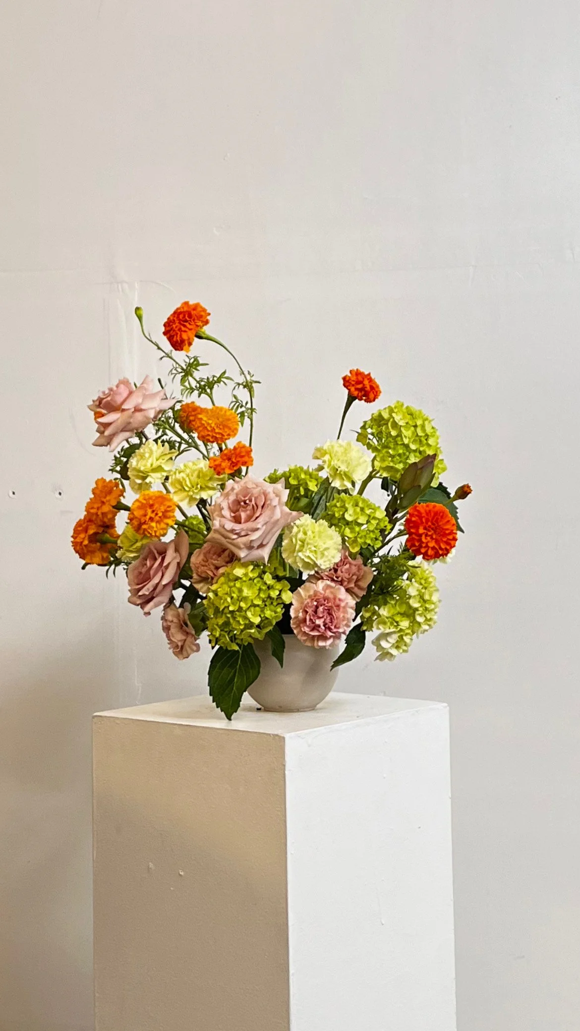 Arrangements florales avec des roses, des hortensias et des œillets dans un vase blanc posé sur un socle blanc