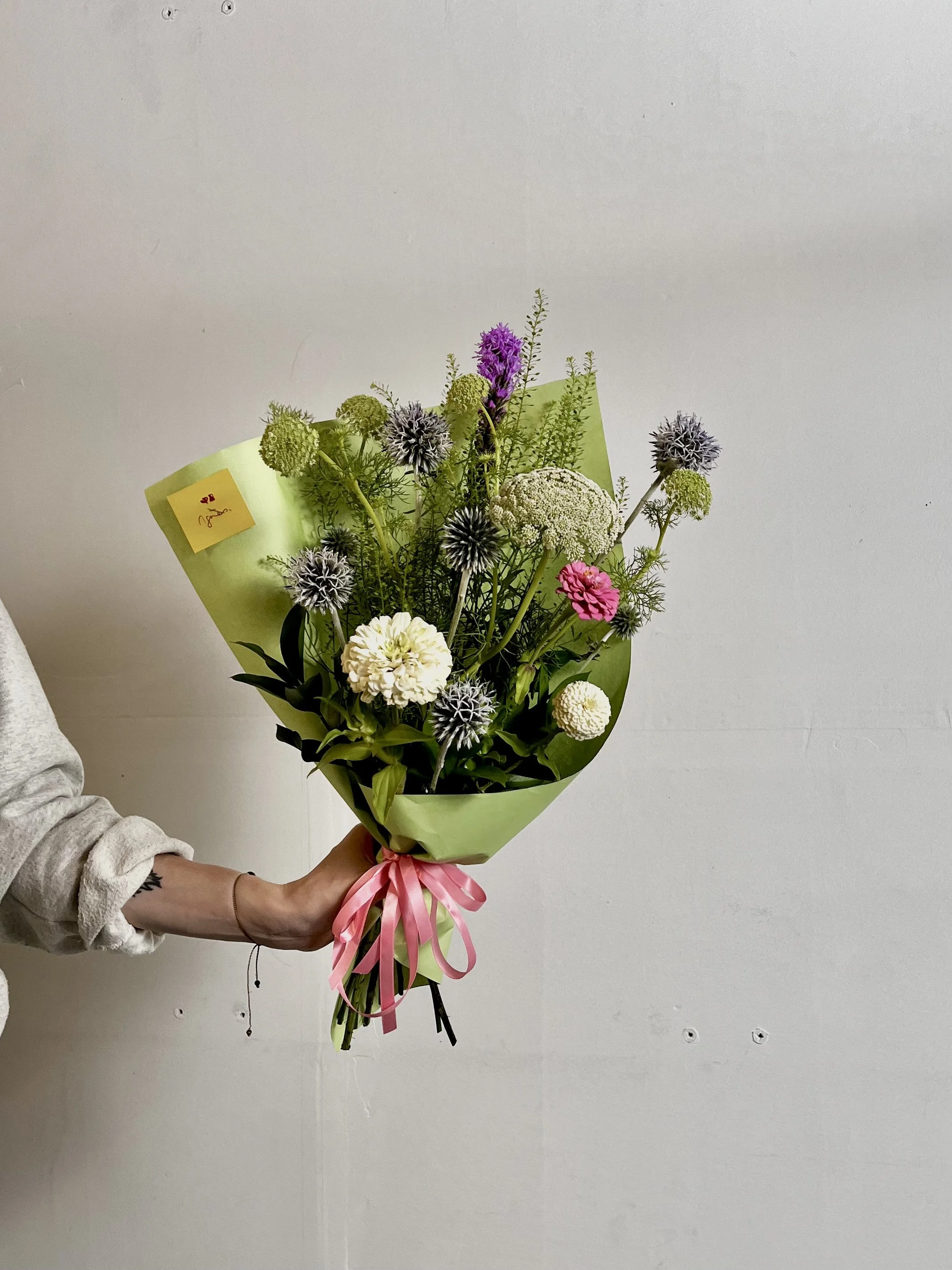 Fleurs colorées et variées dans un bouquet tenu par une personne contre un mur blanc.