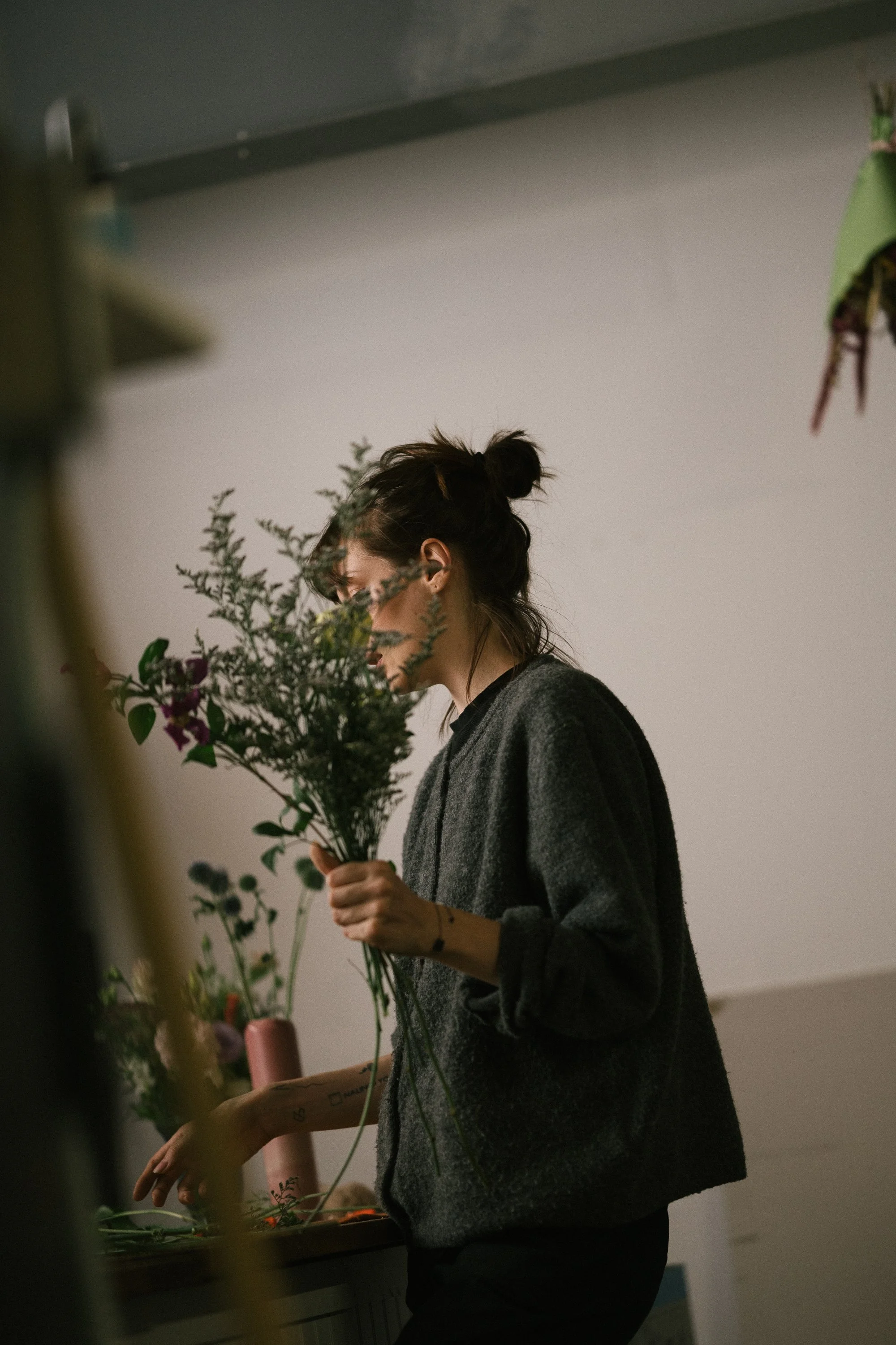 Une femme avec les cheveux attachés en bun, portant un pull gris foncé, tenant un bouquet de fleurs.
