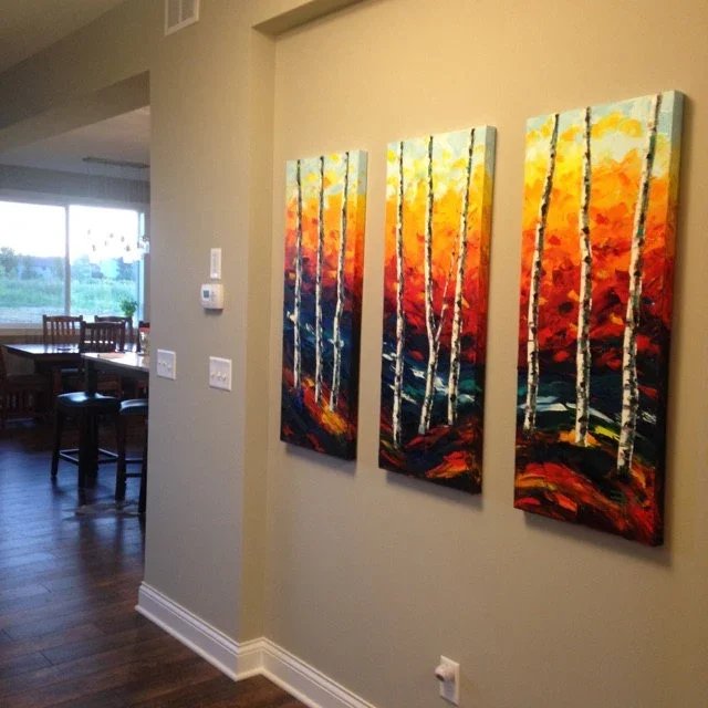 Triptych painting of a colorful autumn forest with white birch trees on a beige wall in a home interior