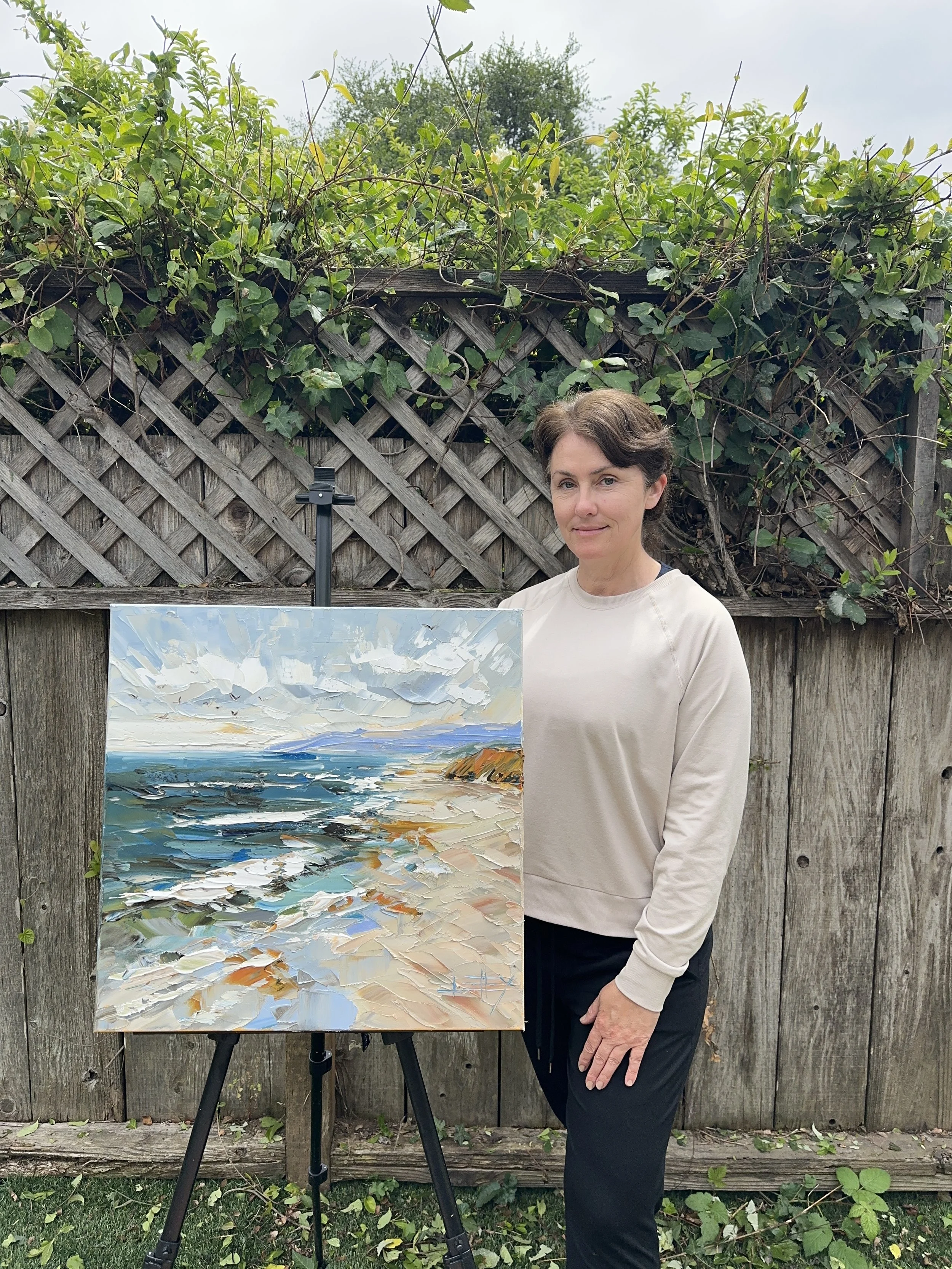 Original palette knife oil painting of the California coast with rolling ocean waves, sandy beach, warm coastal bluff, distant blue headland, and textured sky on gallery wrapped canvas.
