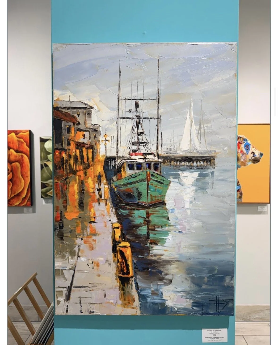 Painting of a waterfront scene with boats docked along a street, colorful reflections on the water, and a cloudy sky.