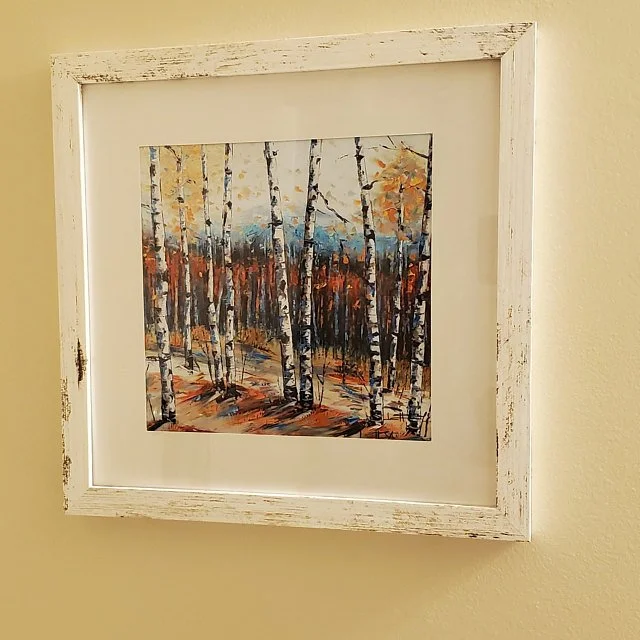 A framed painting of a forest scene with trees and autumn leaves, featuring a mix of orange, yellow, and blue colors.