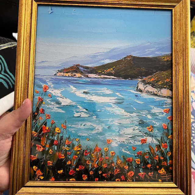 Painting of a coastal landscape with a body of water, hills in the background, and colorful flowers in the foreground.